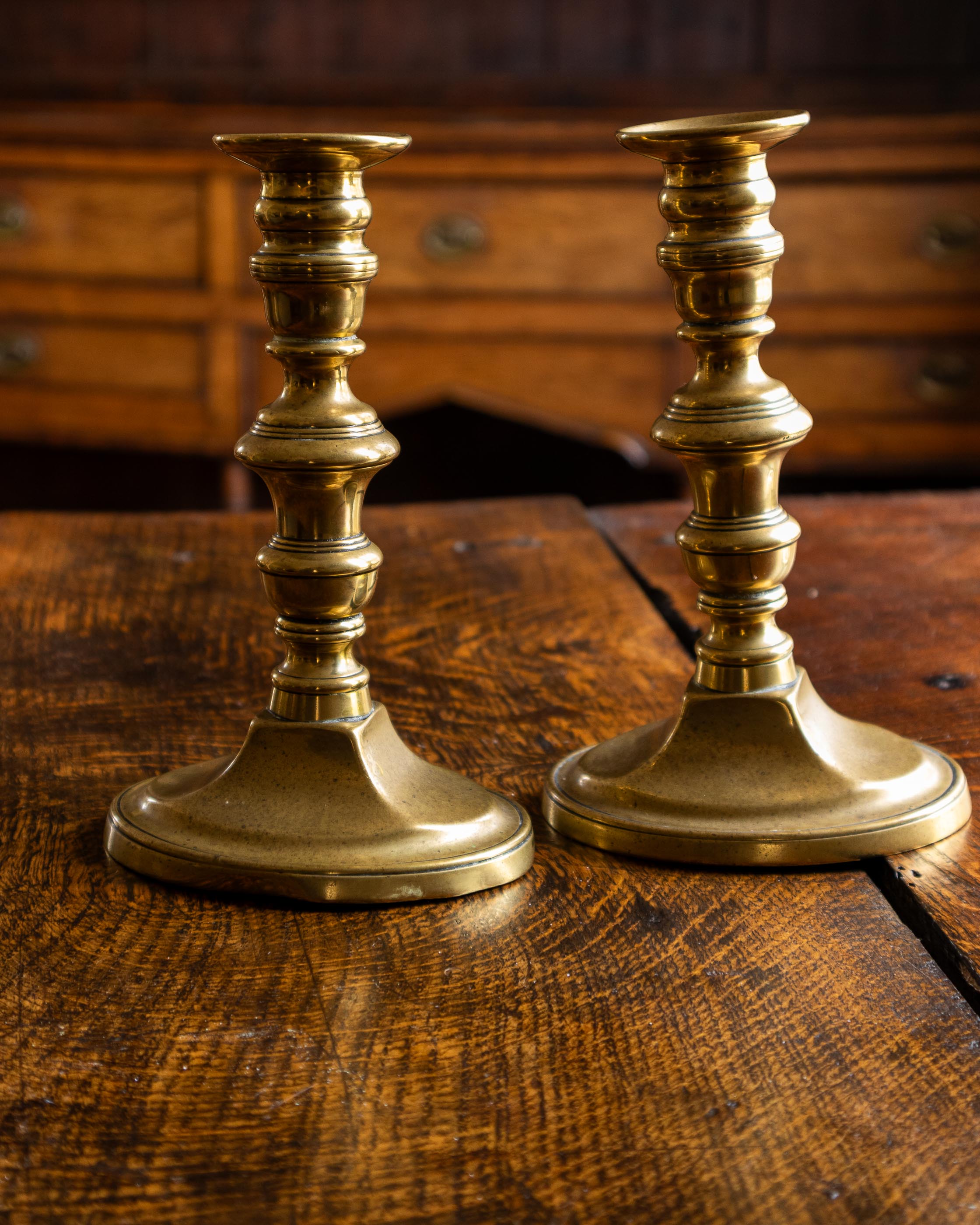 Two brass candlesticks on a wooden surface with a wooden drawer in the background.