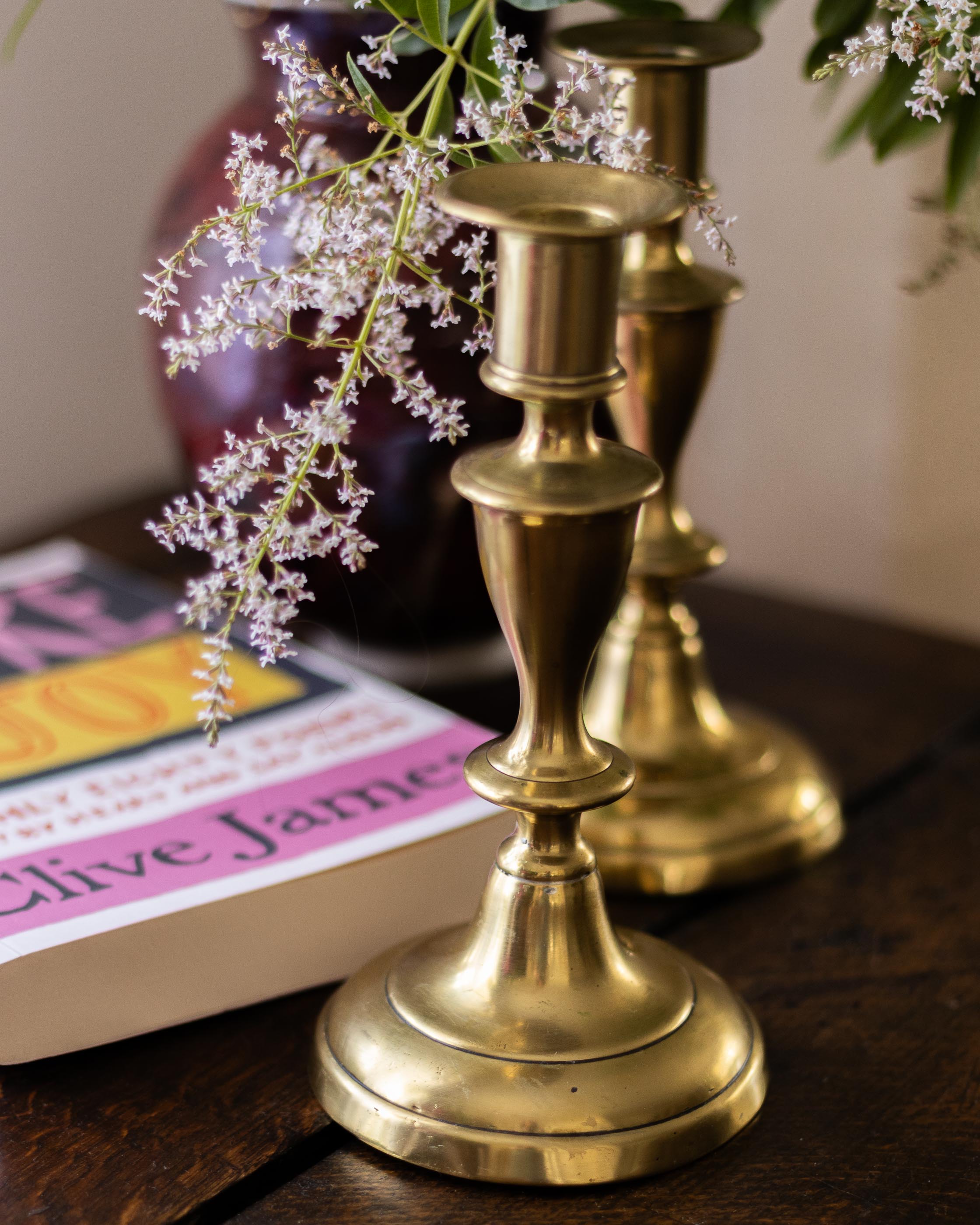 Brass candlestick holders with a book and flowers on a wooden surface