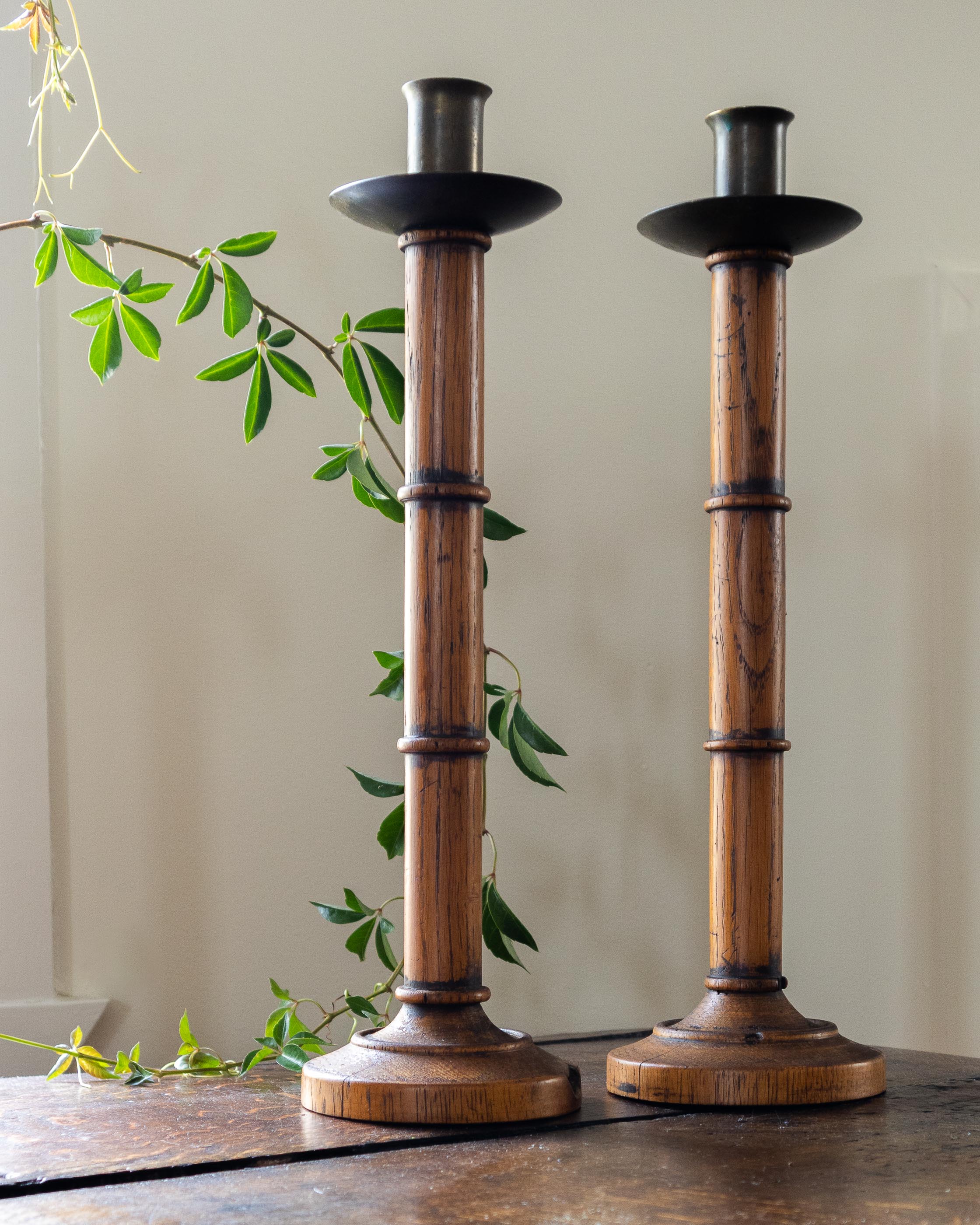 Two wooden candle holders on a table with a plant in the background