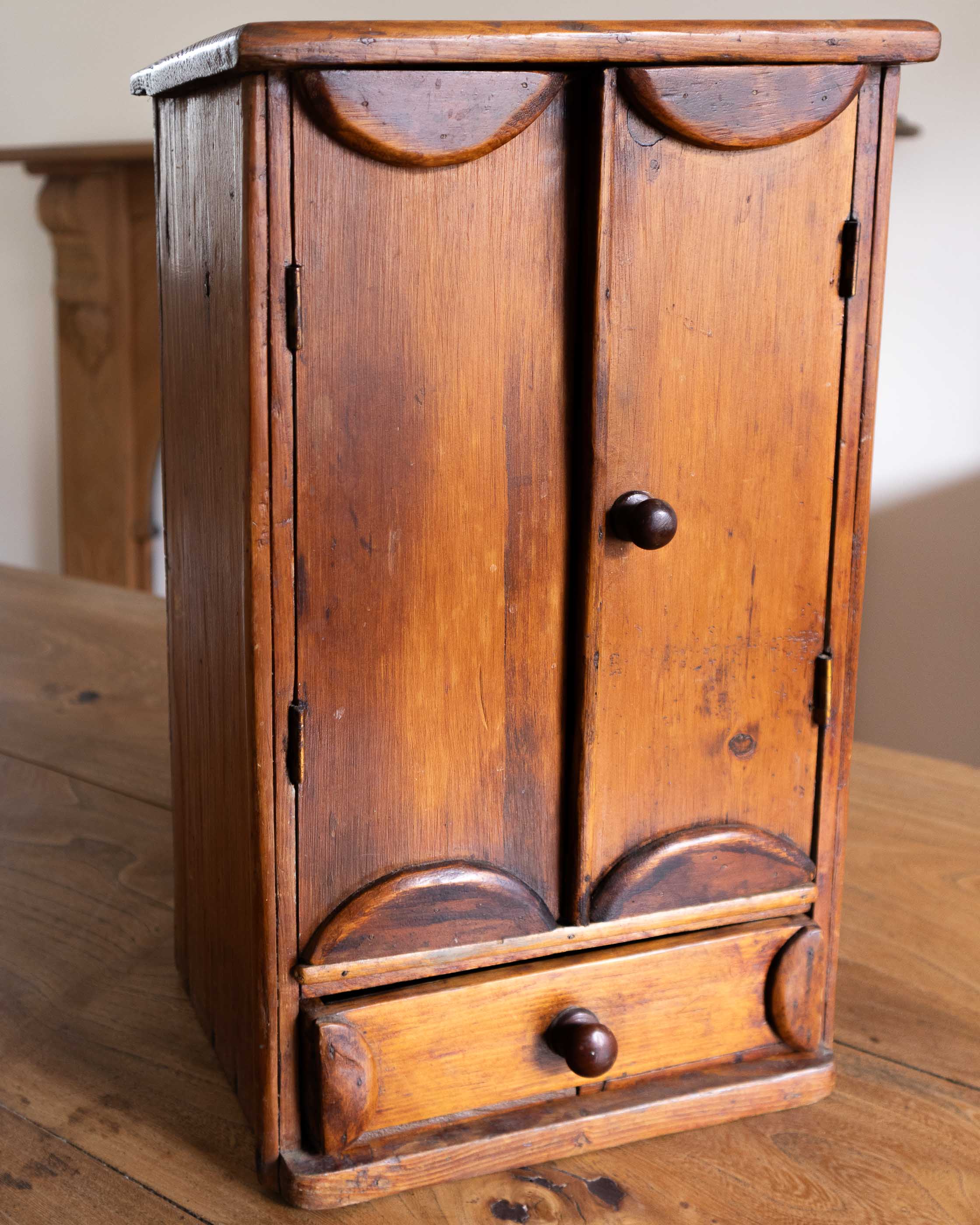 Wooden cabinet with two doors and a drawer on a wooden surface
