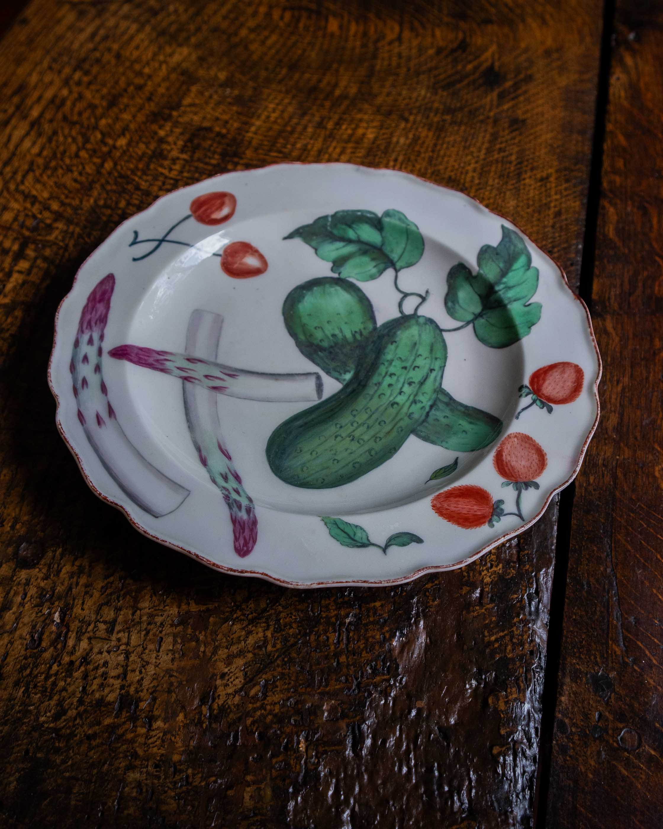 Decorative plate with a cucumber and strawberry design on a wooden surface