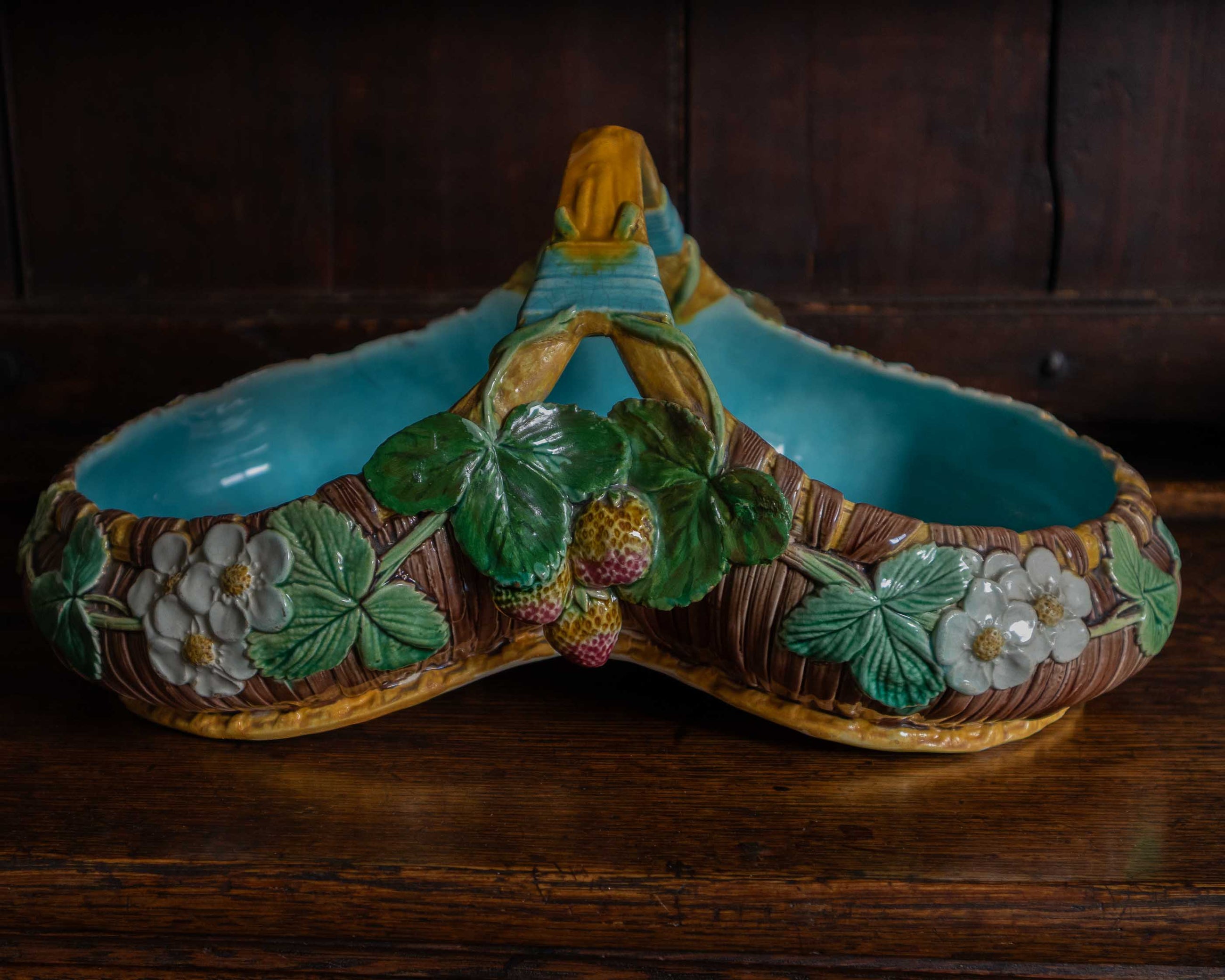 Decorative ceramic basket with floral and berry design on a wooden surface