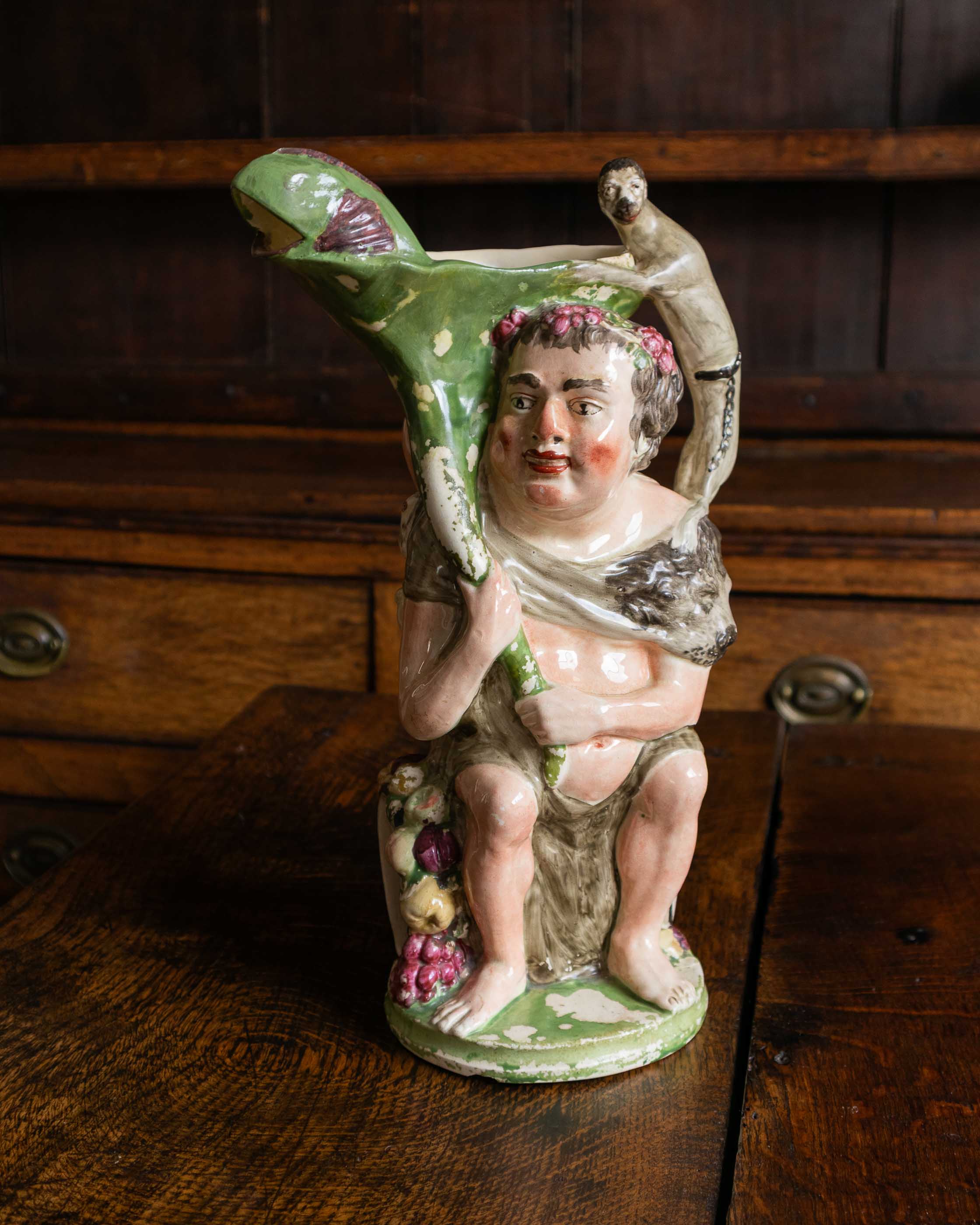 Vintage ceramic figure of a bacchus placed on a wooden surface.