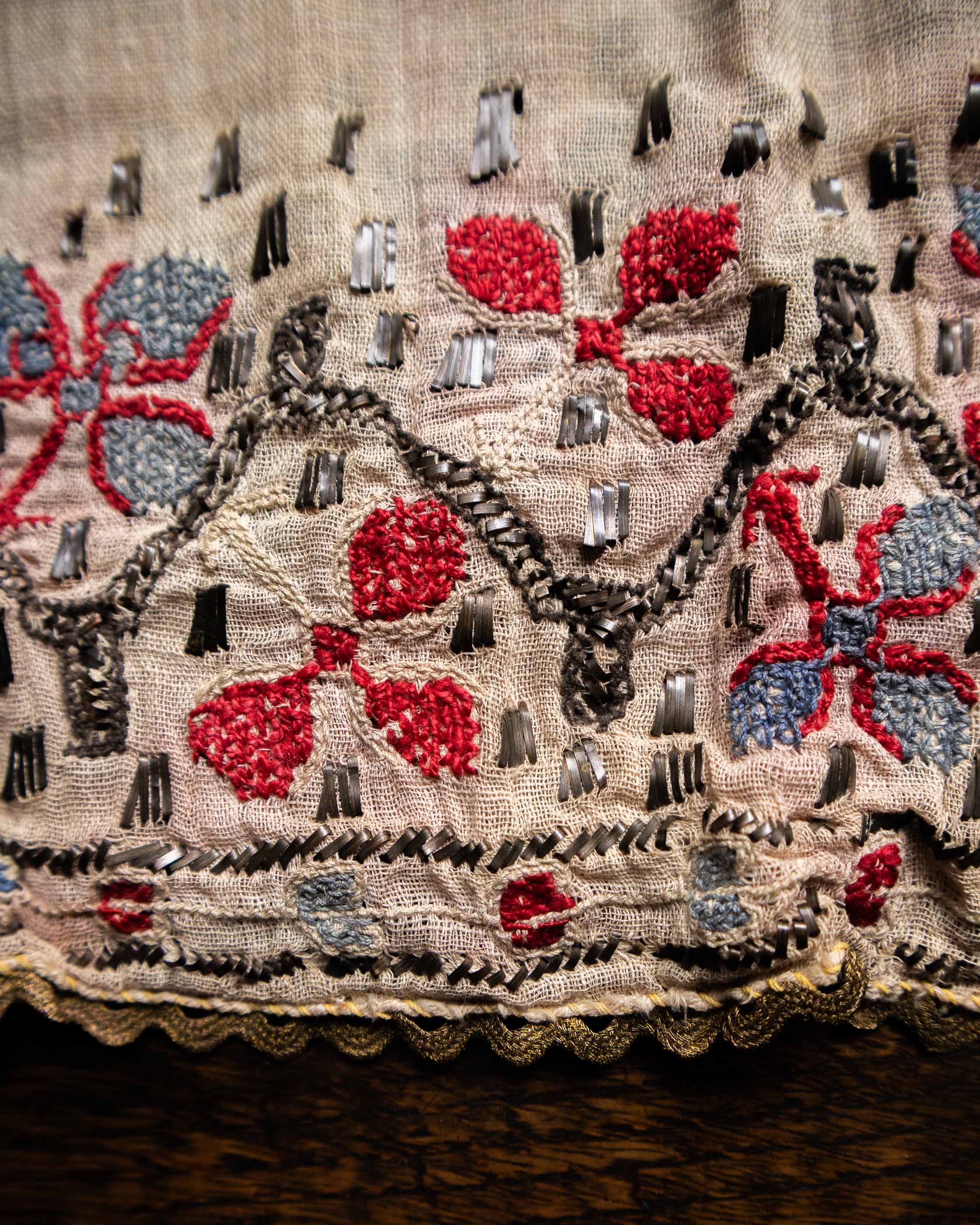 Close-up of embroidered fabric with red flowers, black and gray patterns on a beige background