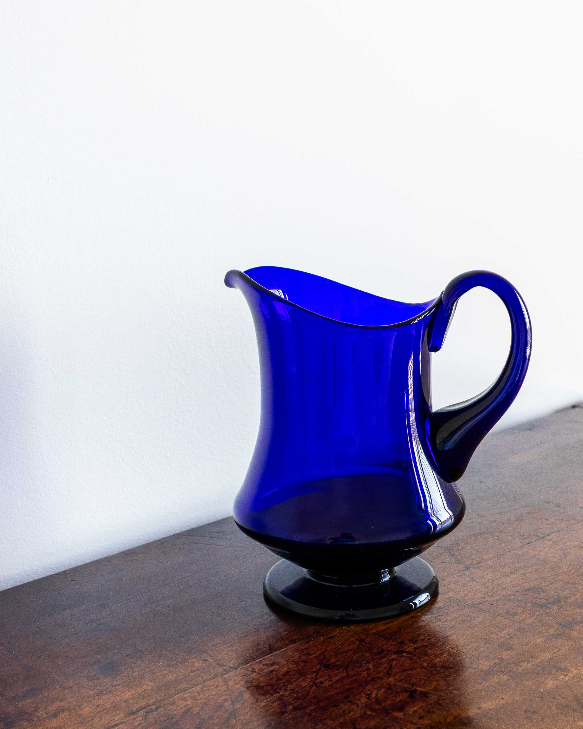 Blue glass pitcher on a wooden surface with a white background