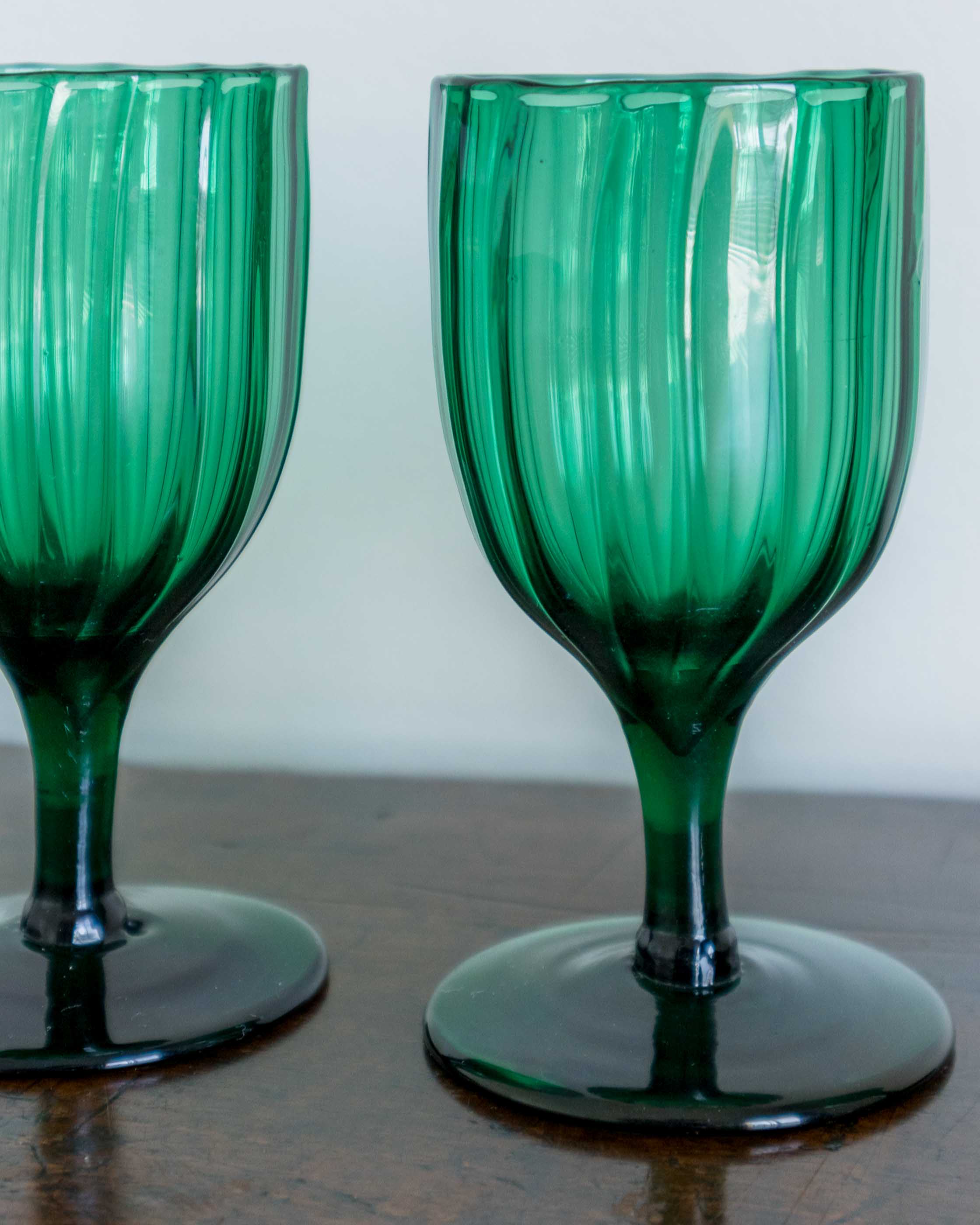 Two green glass goblets on a wooden surface with a white background