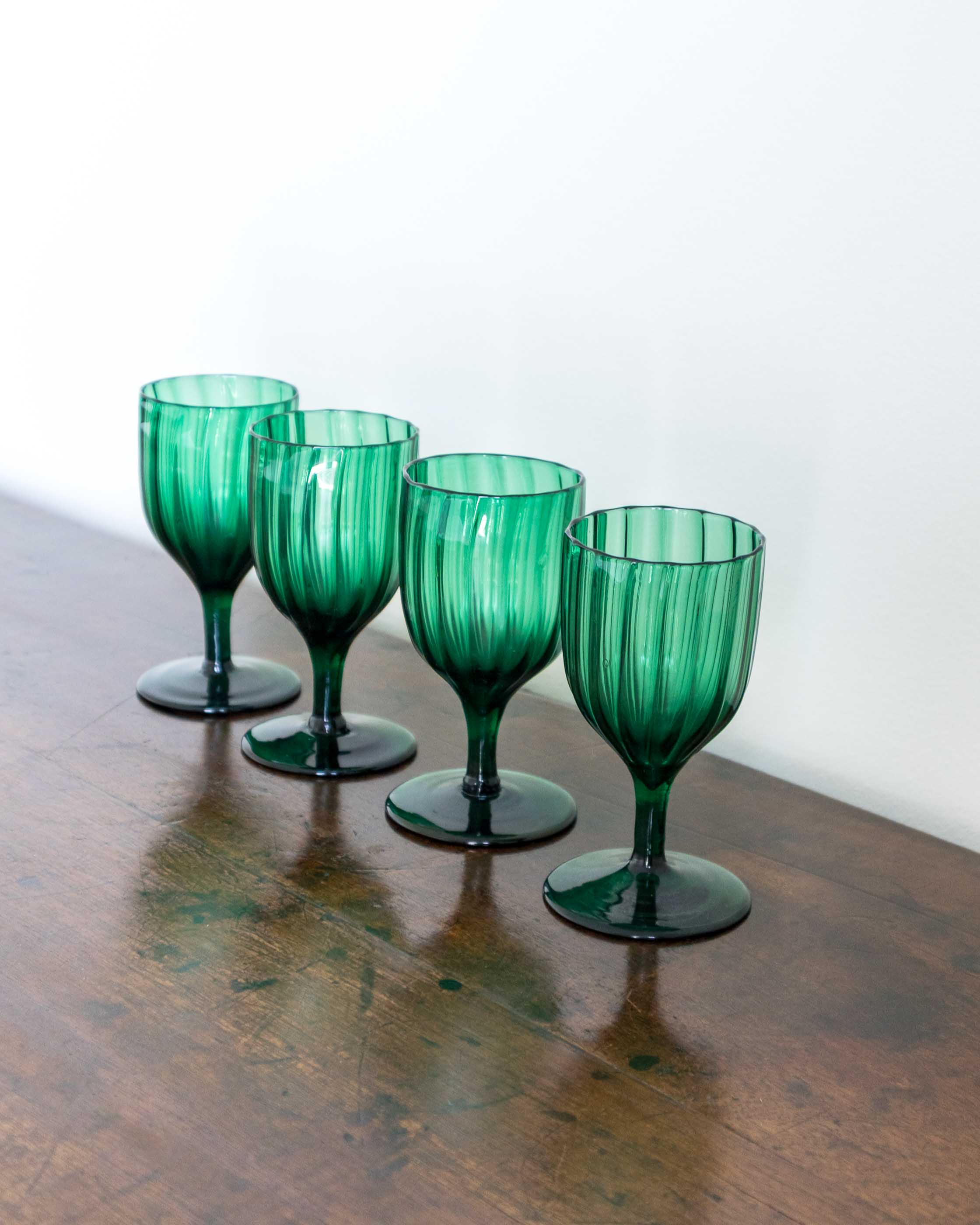 Four green glass goblets on a wooden surface with a white background