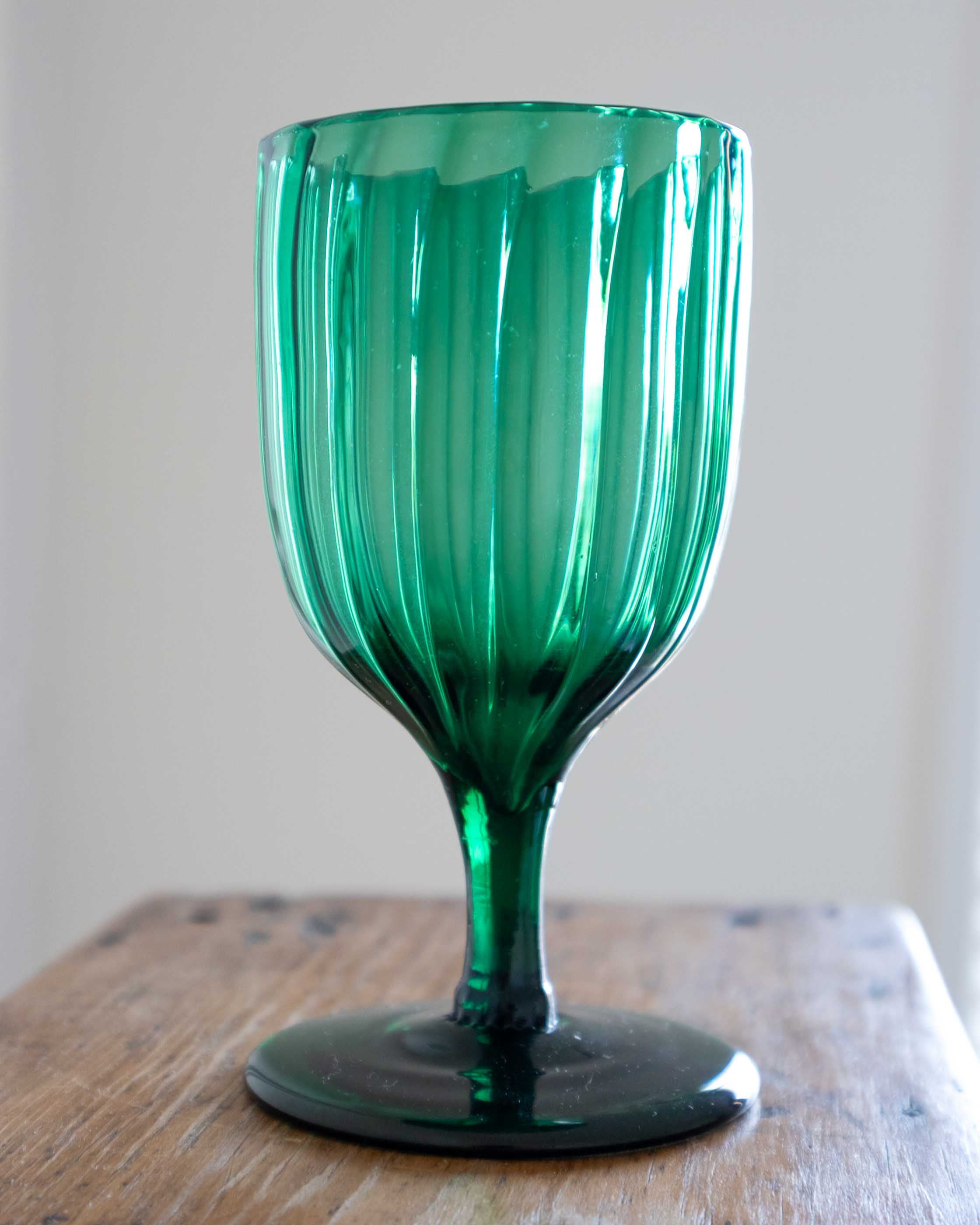 Green glass goblet on a wooden surface with a neutral background