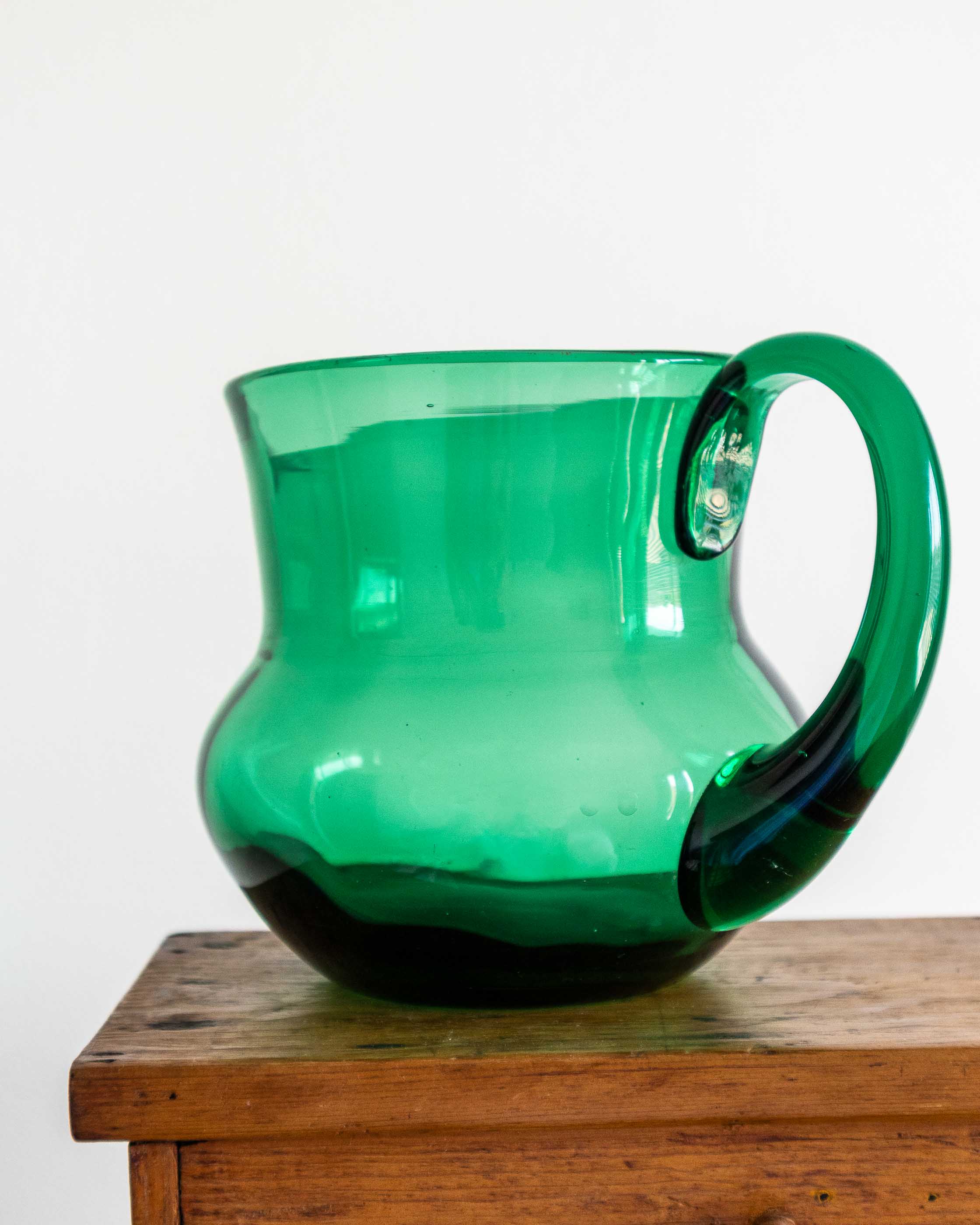 Green glass pitcher with handle on a wooden surface