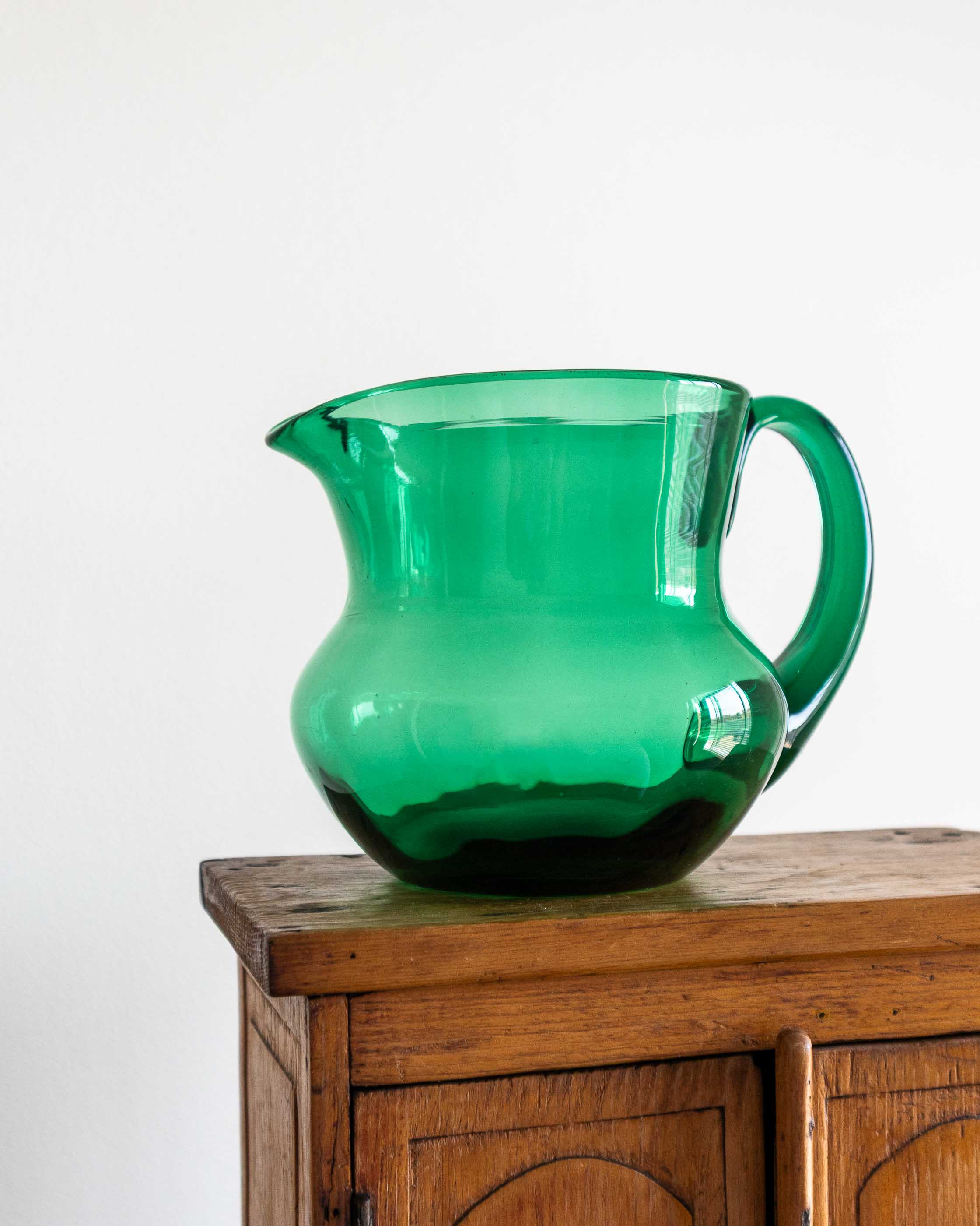 Green glass pitcher on a wooden cabinet against a white background