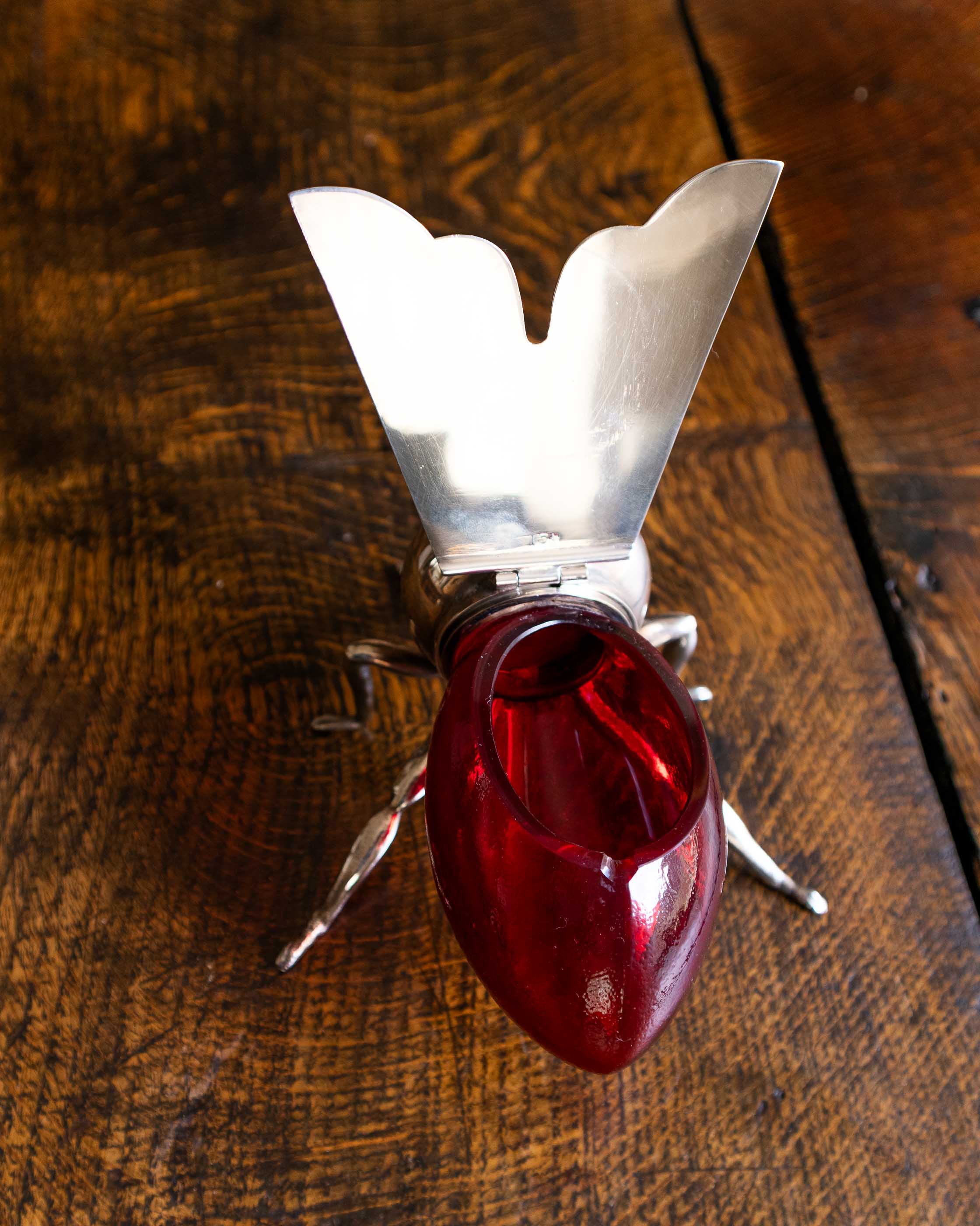 Decorative bee honey pot with a red glass base and metal legs on a wooden surface