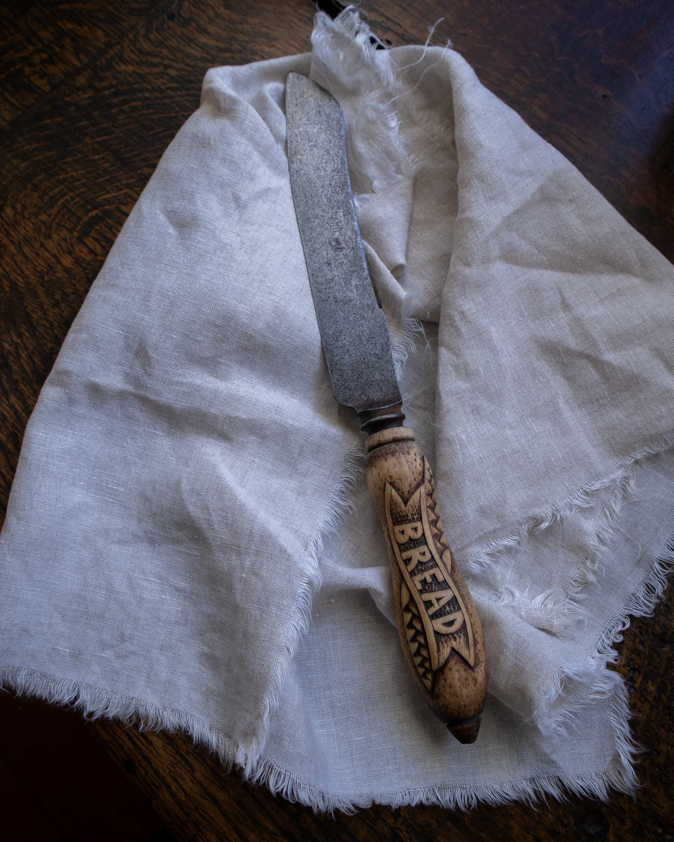 Bread knife with wooden handle on a white cloth on a wooden surface