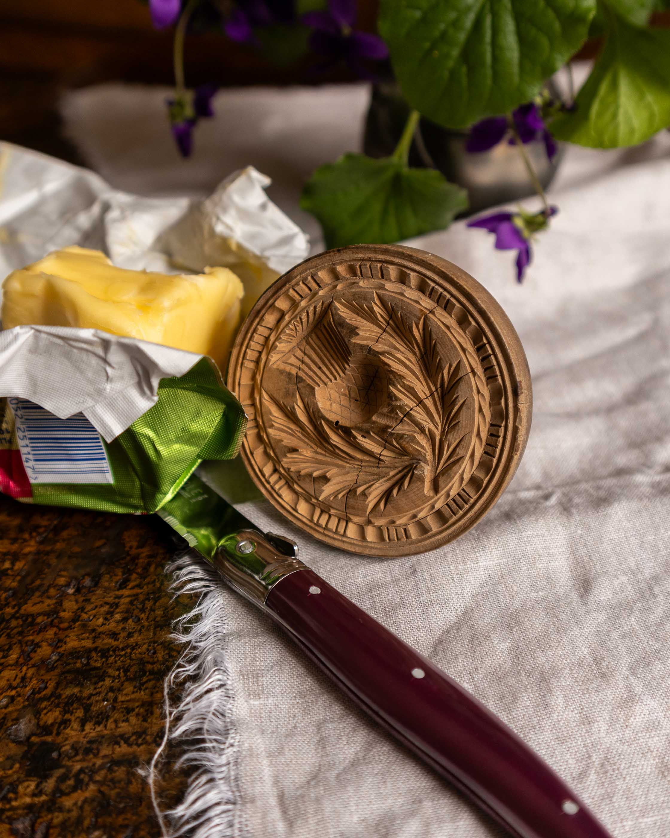 Wooden butter stamp with floral design on a textured surface with a knife and butter.