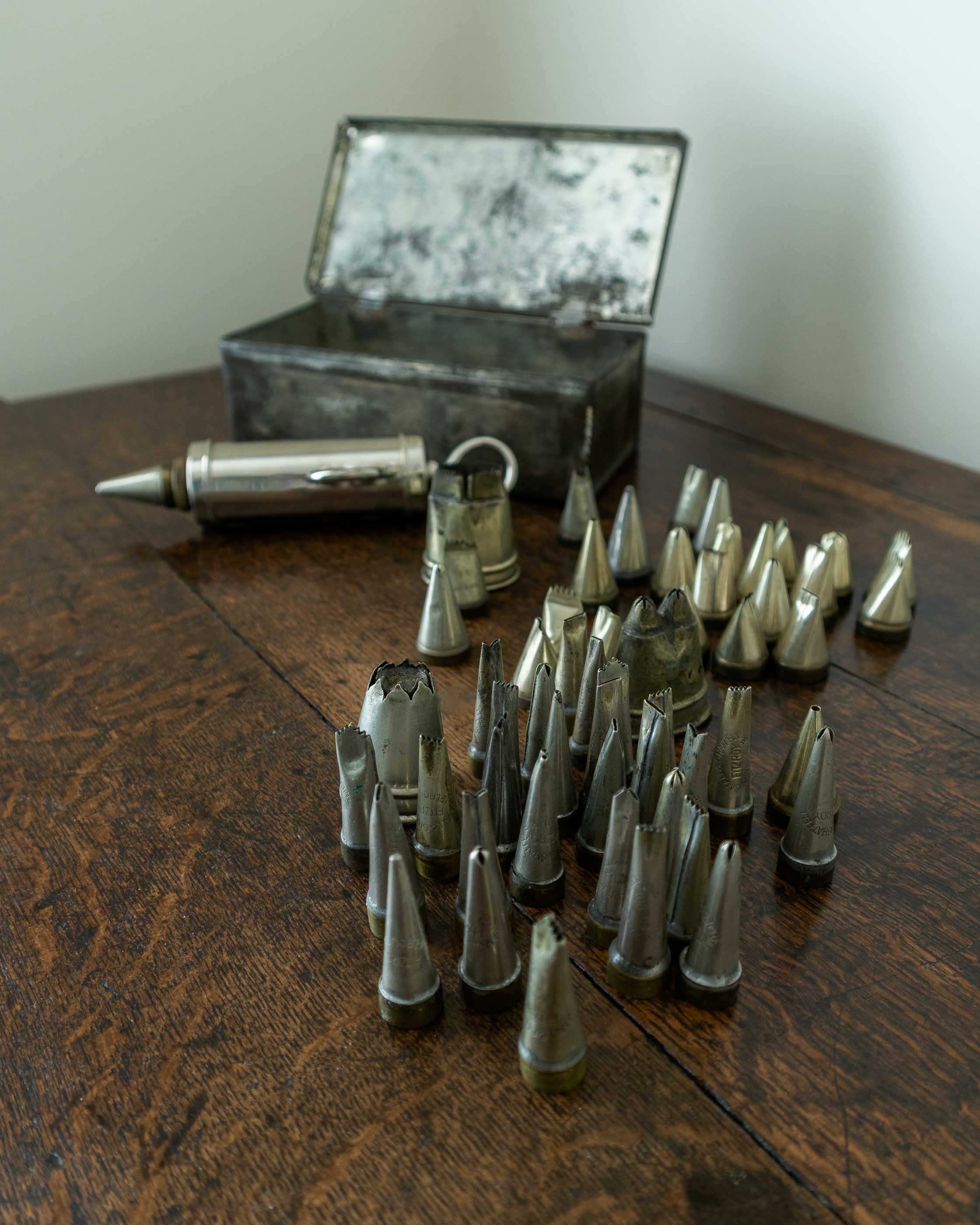Collection of metal icing nozzles and a metal container on a wooden surface.