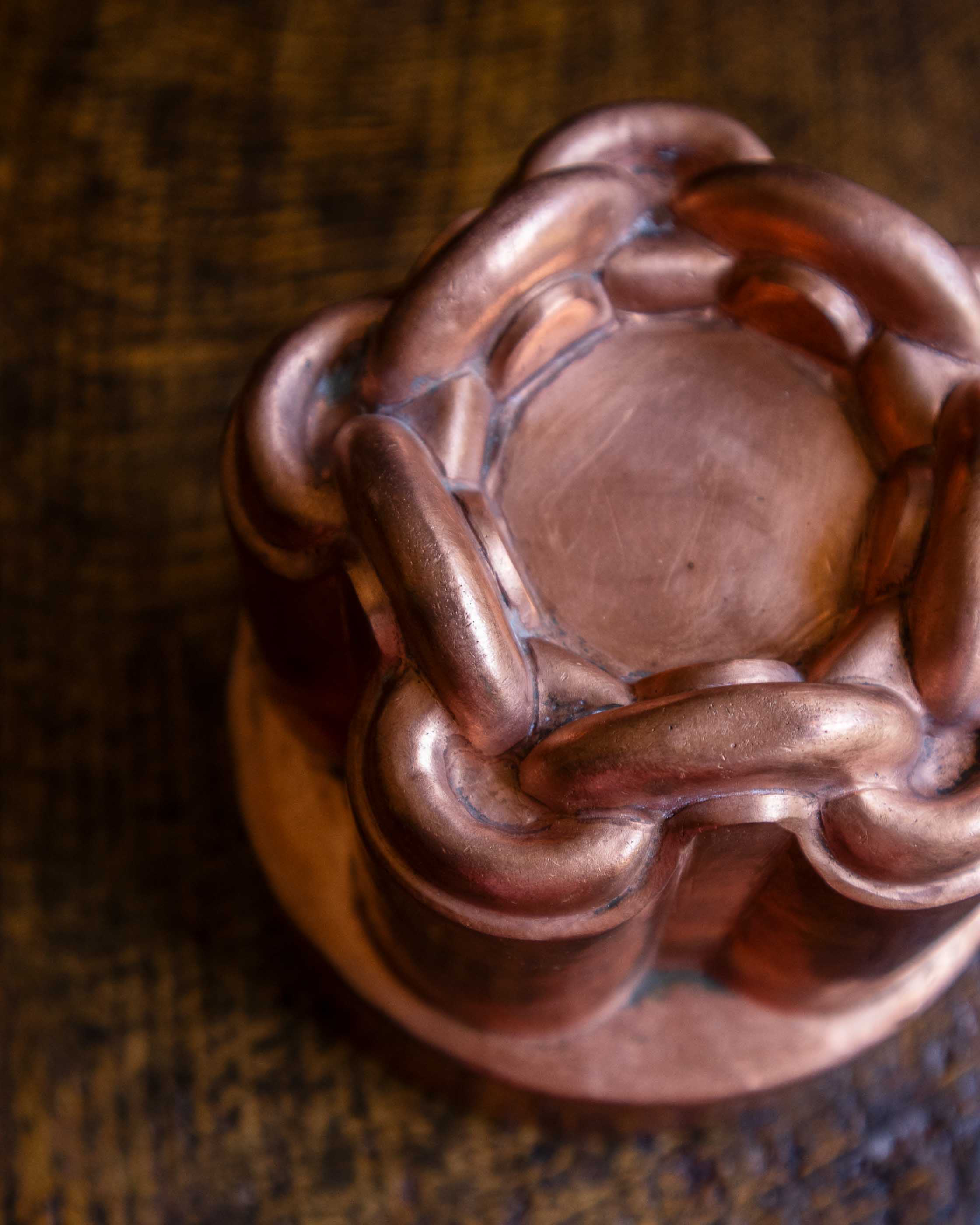 Close-up of a copper chain knot jelly mould on a wooden surface.