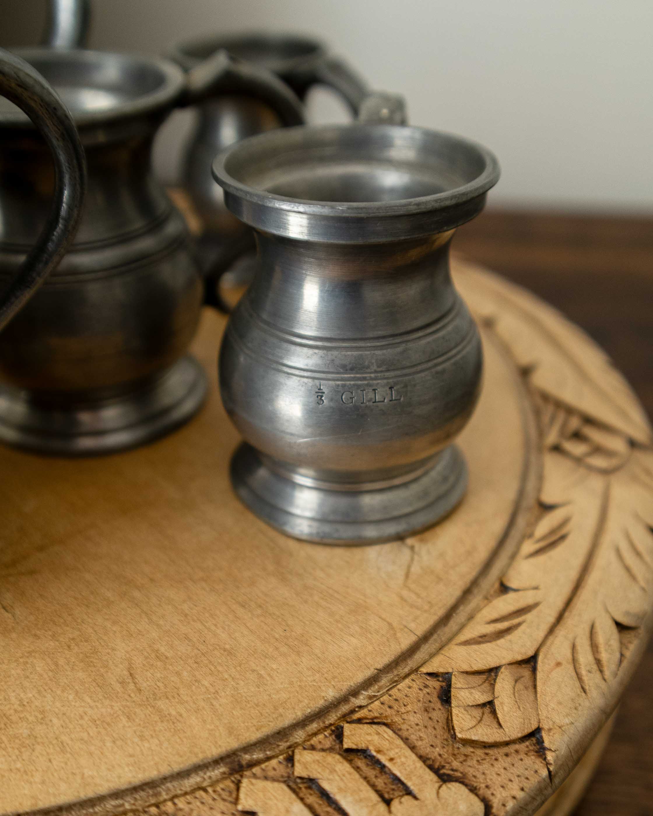 Pewter measures on a wooden breadboard with intricate carving
