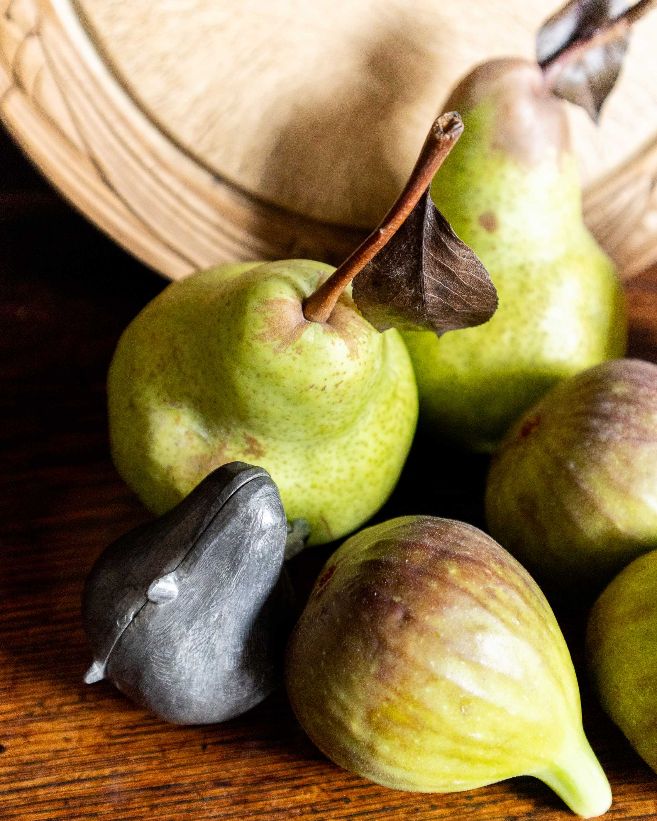 Green pears and figs on a wooden surface with a pewter mould.
