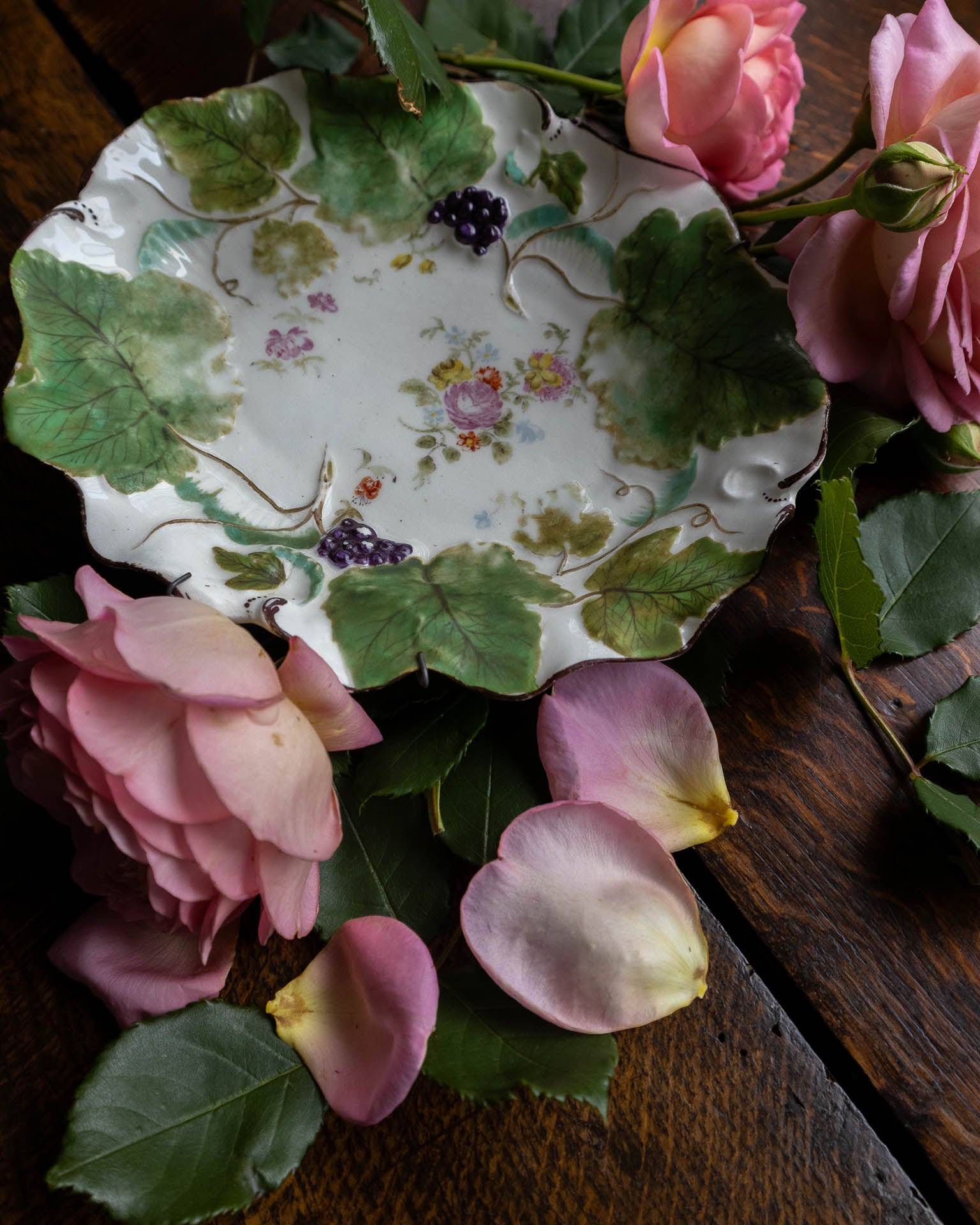 Decorative ceramic Derby porcelain dish with floral design on a wooden surface with flowers and leaves.