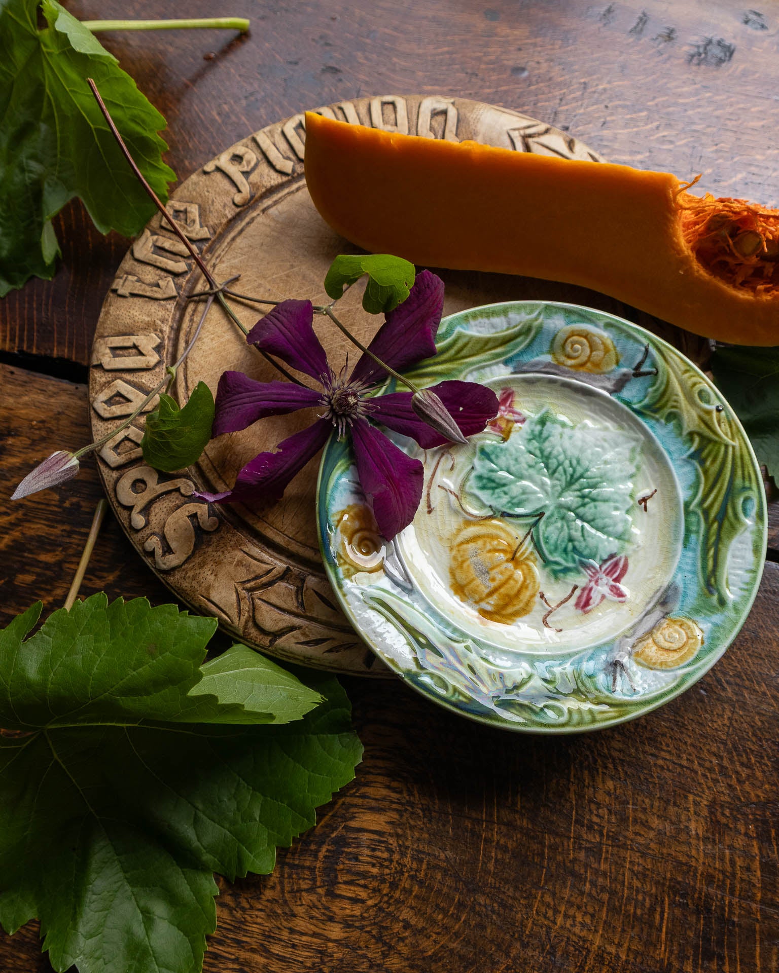 Decorative ceramic plate with floral design on a wooden surface with leaves and a pumpkin.