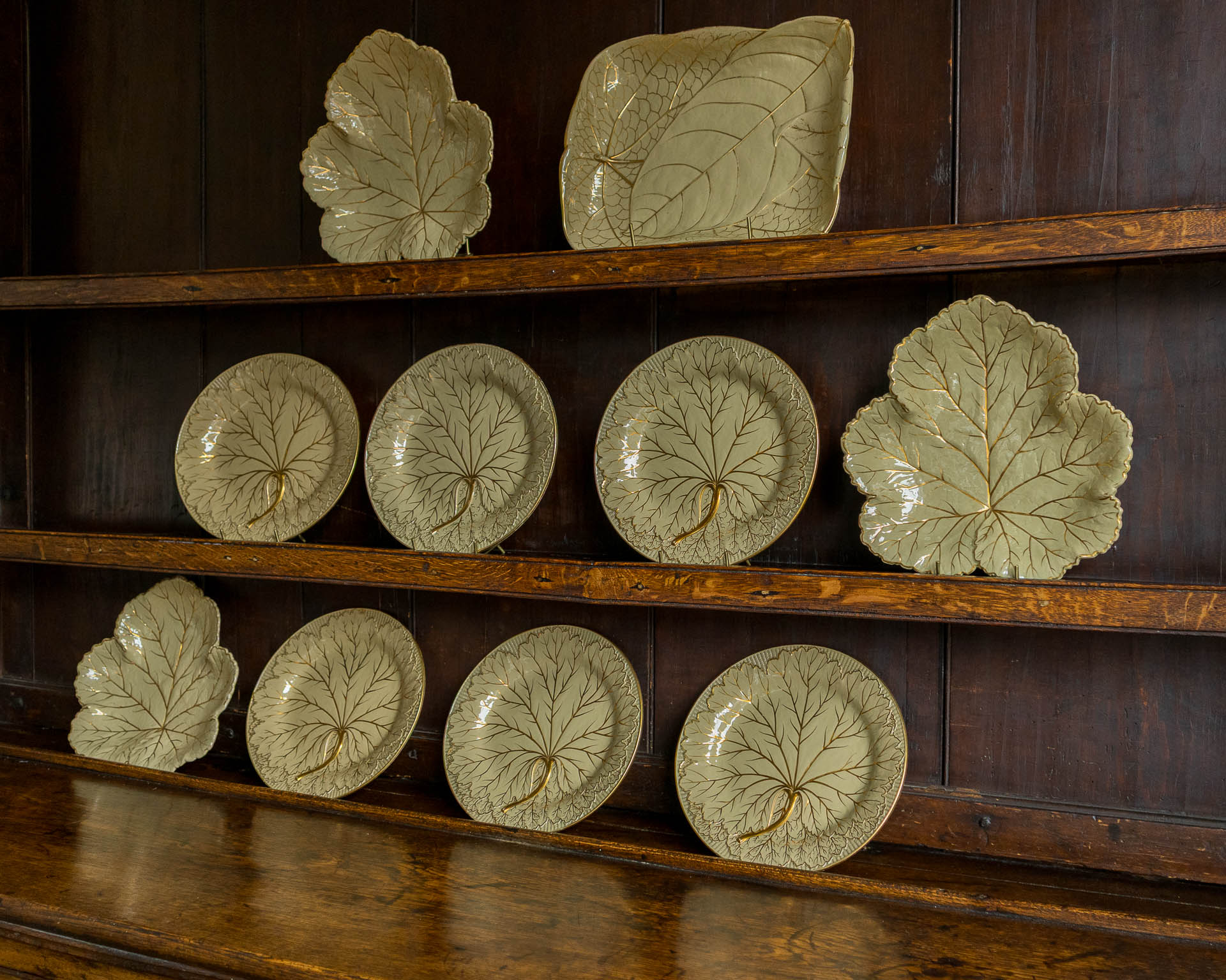 Set of ceramic Wedgwood leaf-shaped plates on wooden shelves.