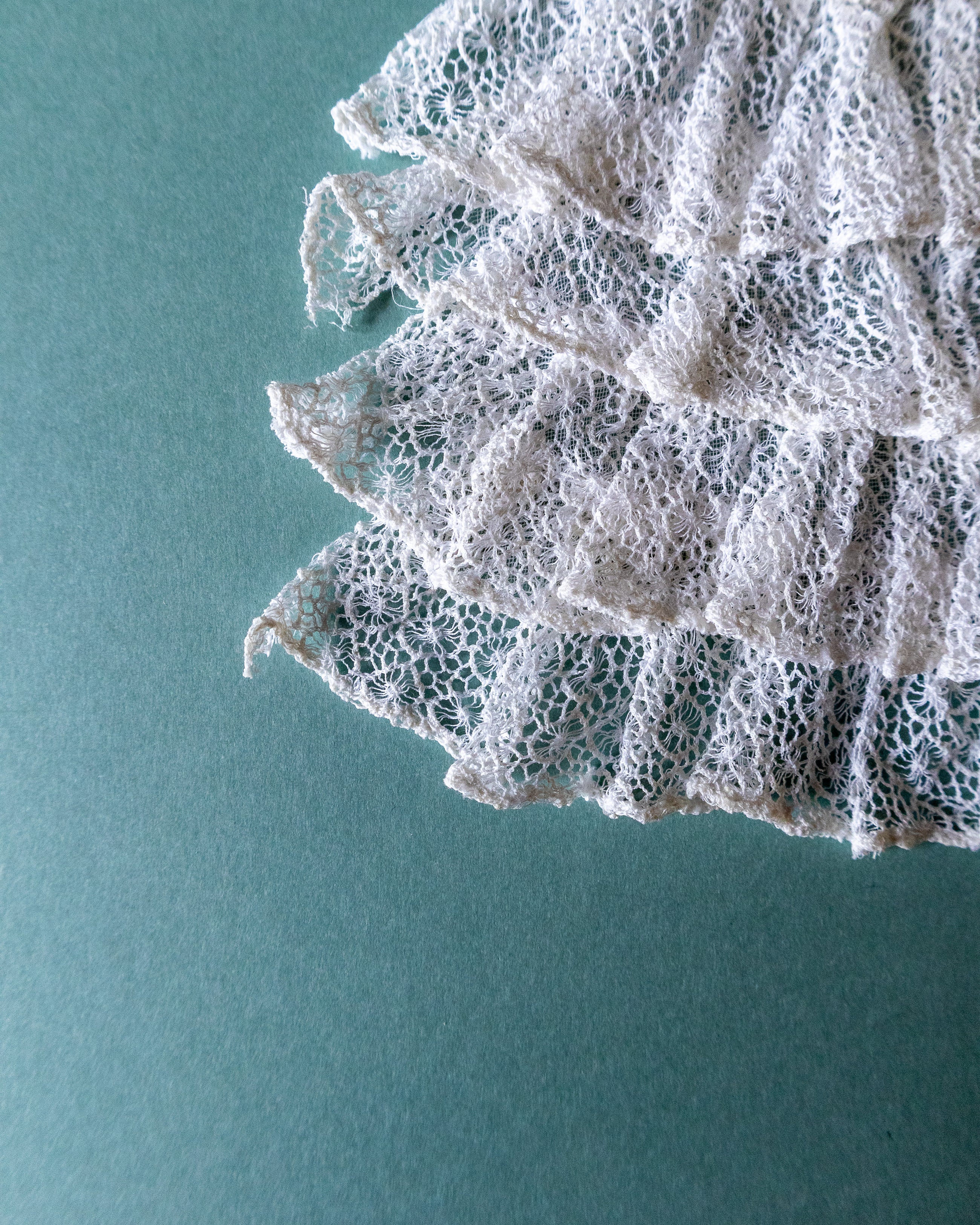 Close-up of lace fabric corner on a teal background