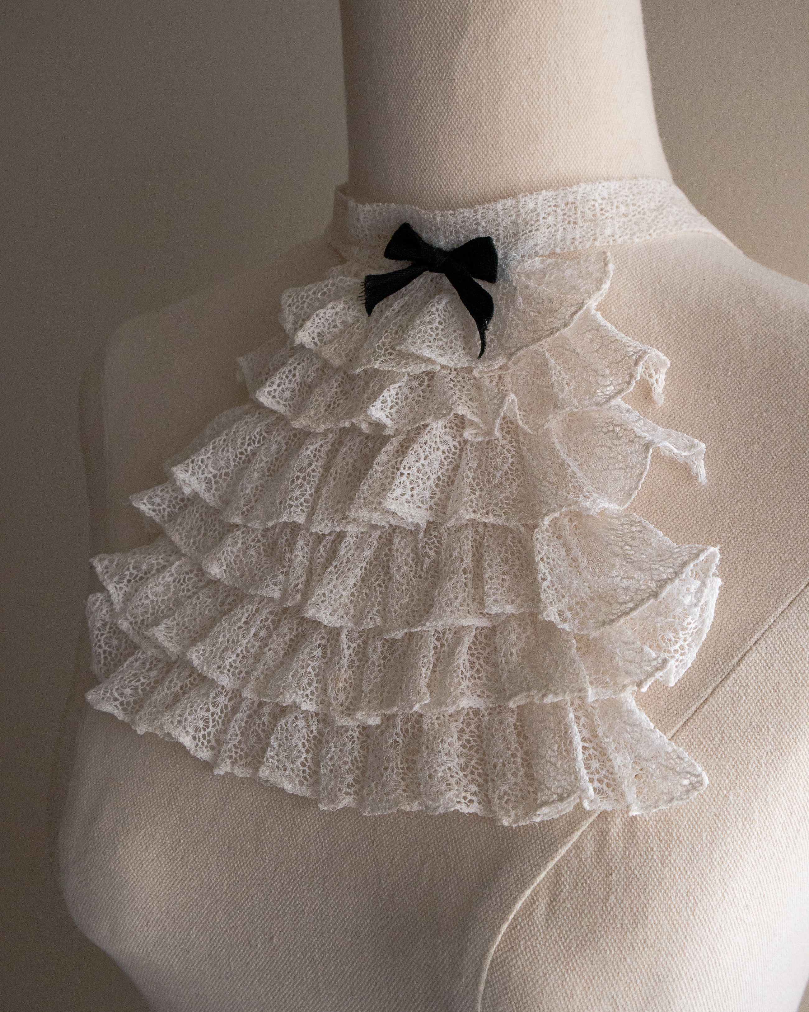 White lace jabot with a black bow on a mannequin against a neutral background