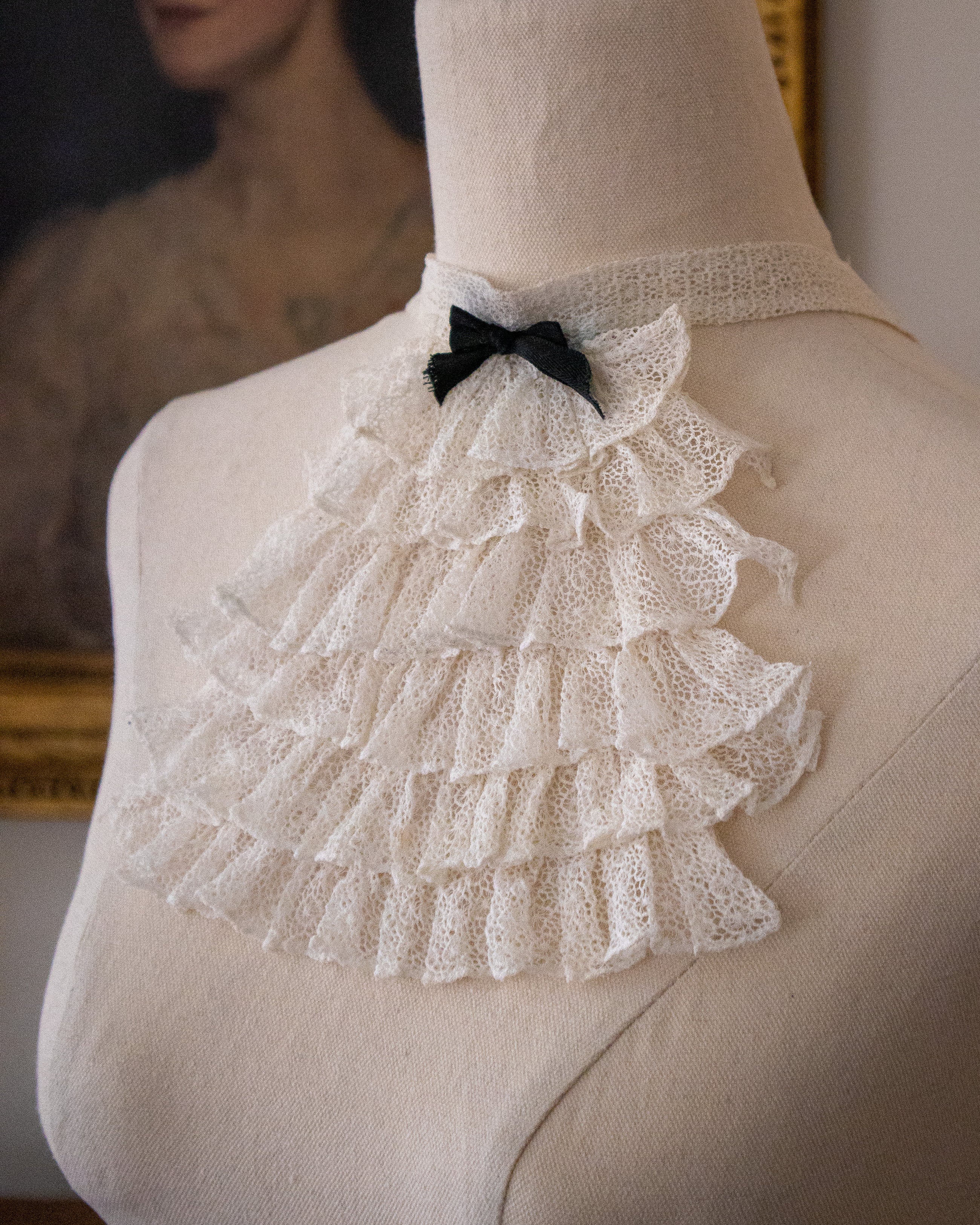 Mannequin wearing a white lace jabot with a black bow tie