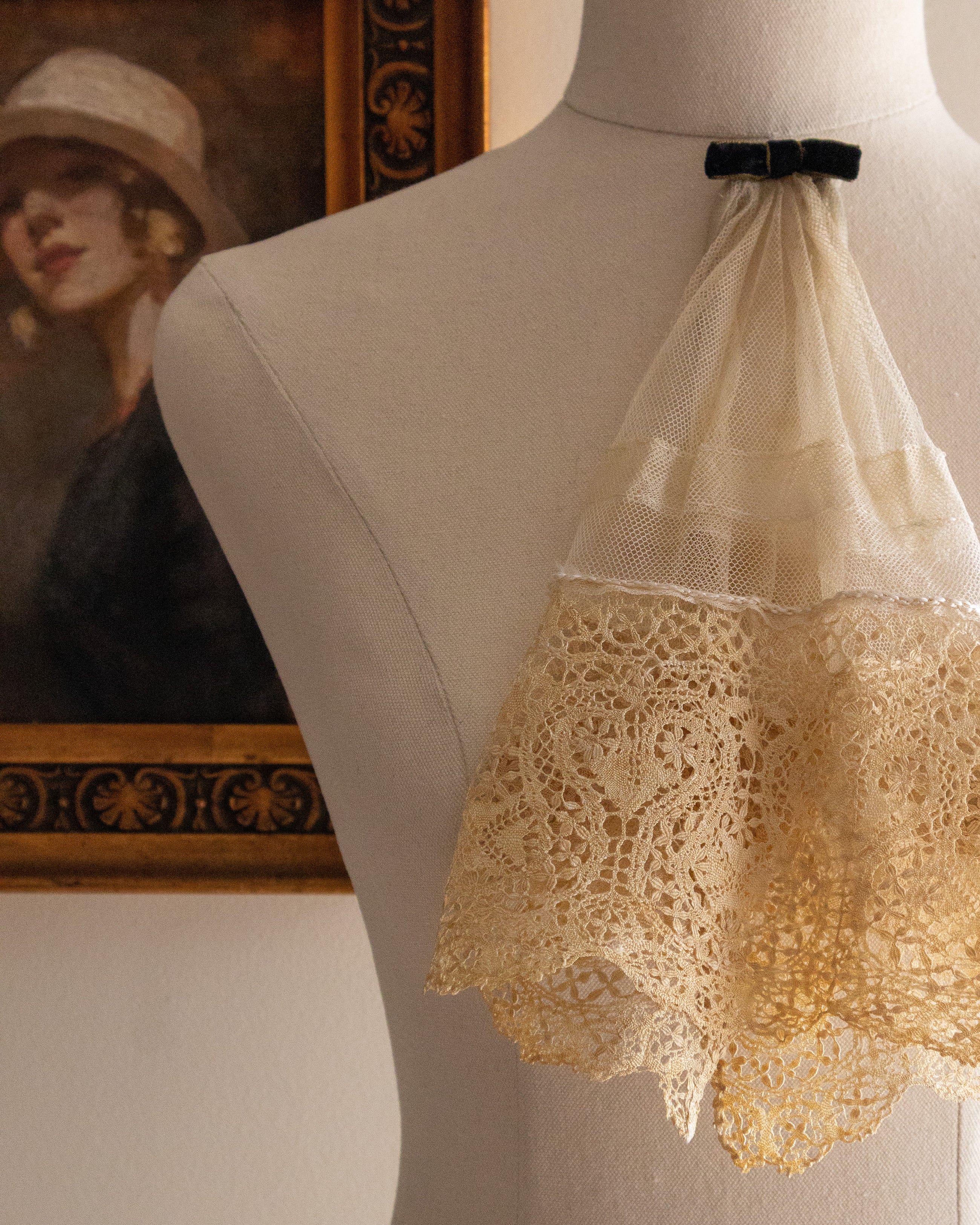 Mannequin wearing a lace jabot with a painting in the background
