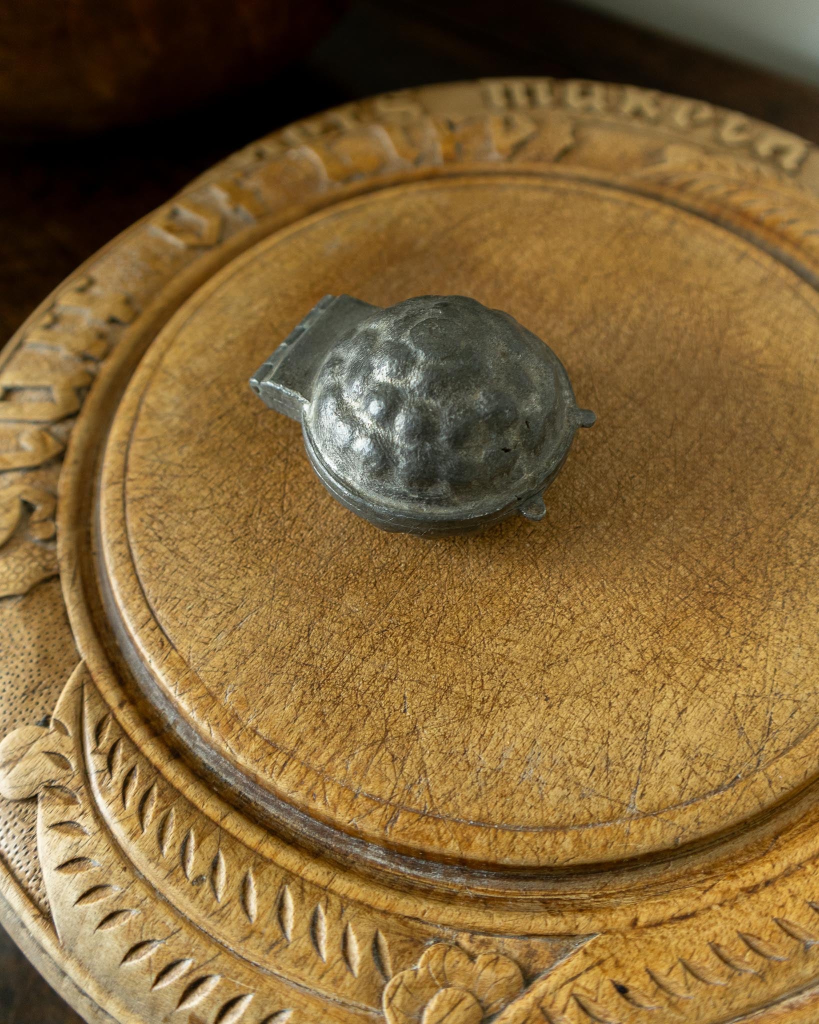 Decorative wooden breadboard with a pewter mould on a dark background