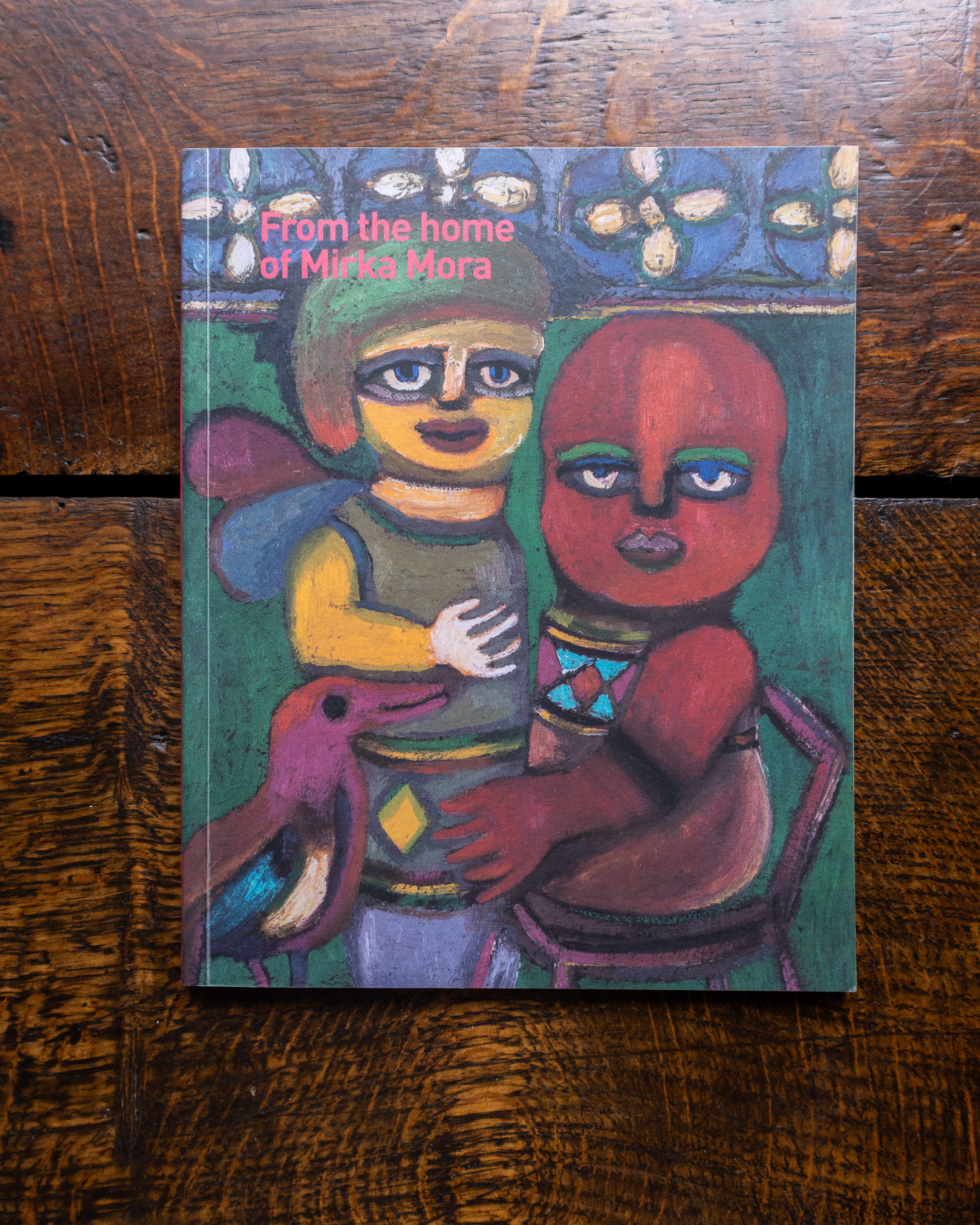 Book cover with colorful painting by Mirka Mora of two figures and a dog on a wooden surface