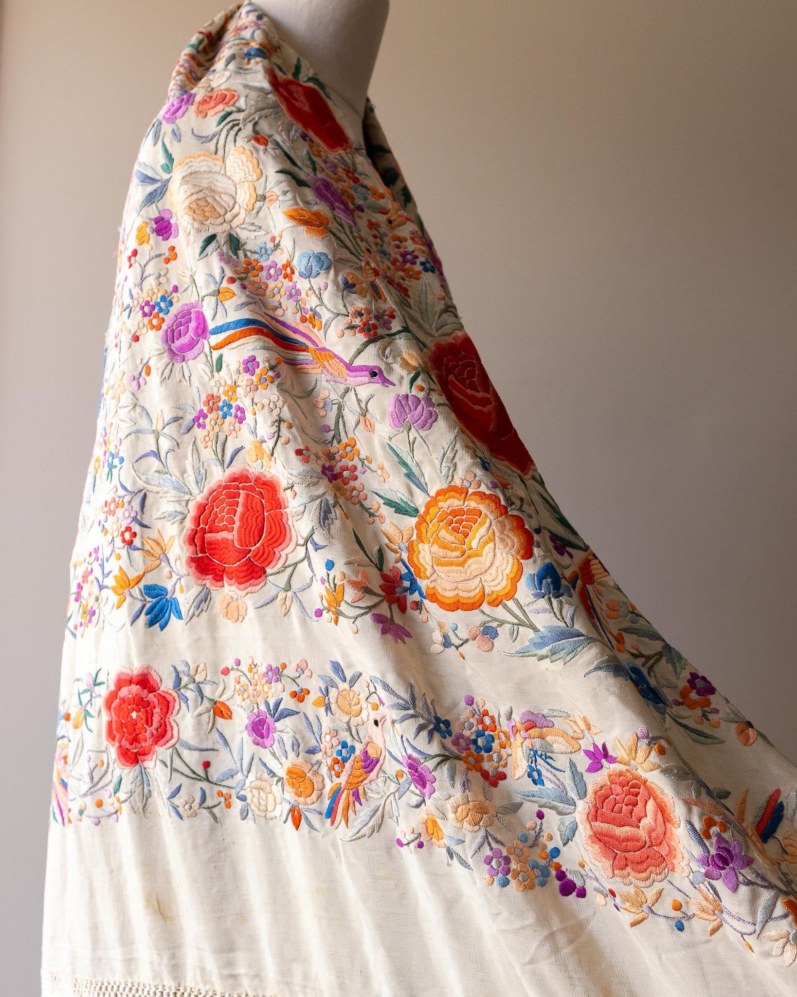 Colorful floral antique Chinese silk shawl draped over a mannequin against a neutral background