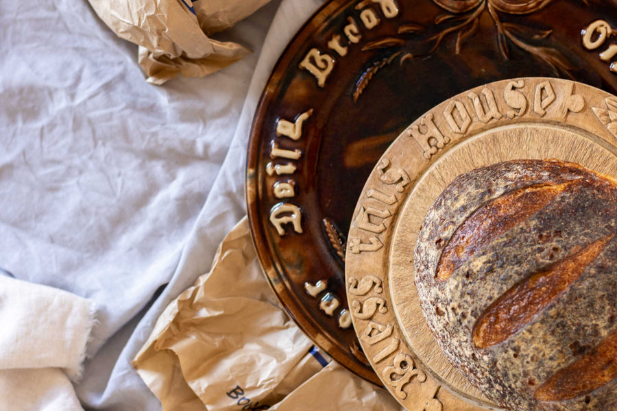 Antique breadboard and plate with sourdough bread loaf on a table with a light cloth
