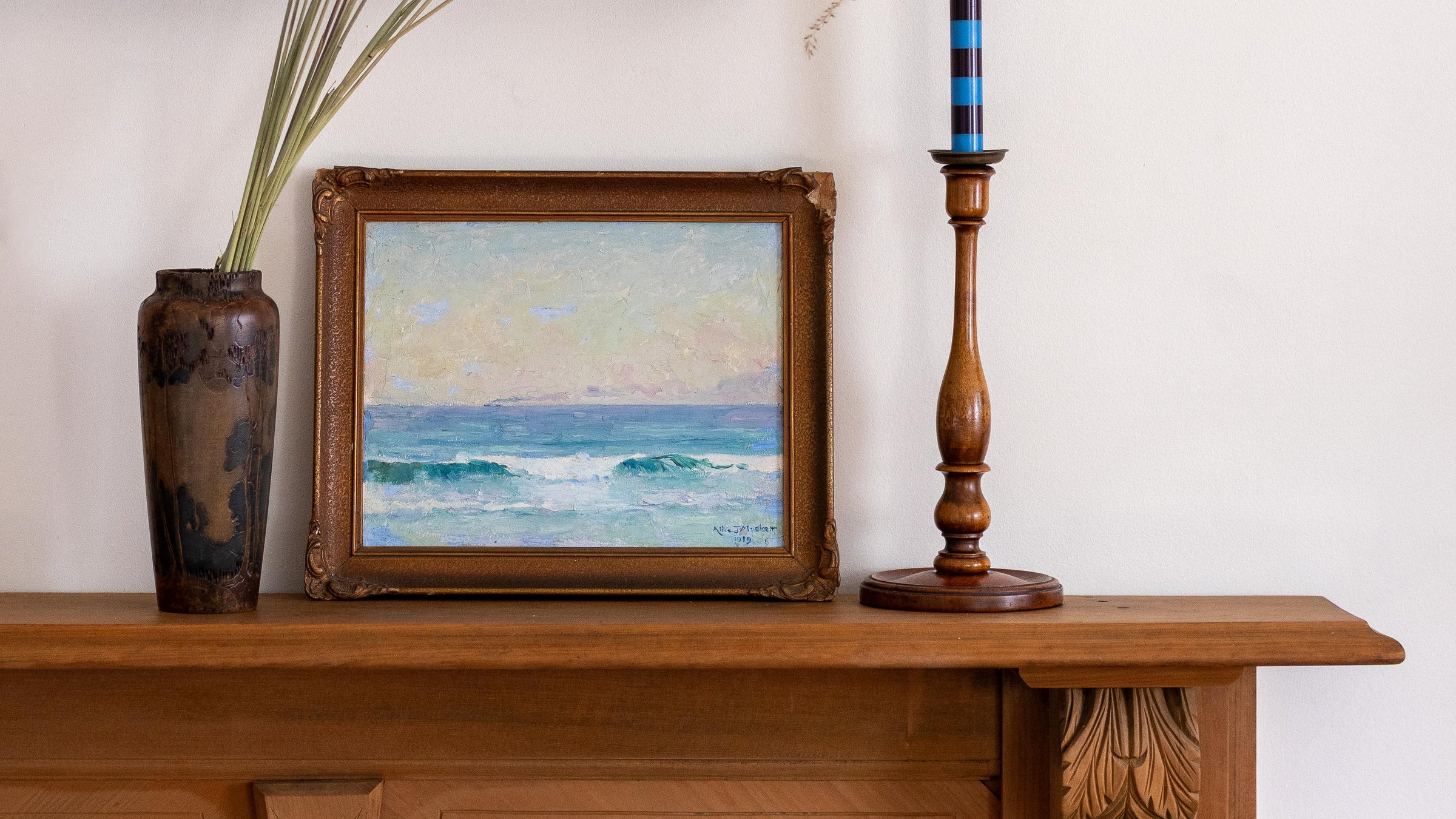 Framed painting of a seascape on a wooden shelf with a vase and candlestick.