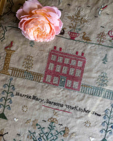 Embroidered cross stitch antique sampler with a house design and a pink flower on top