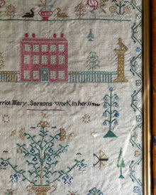 Embroidered sampler with a house, trees, and text on a beige background