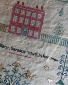 Embroidered cross stitch sampler with a house and text on fabric