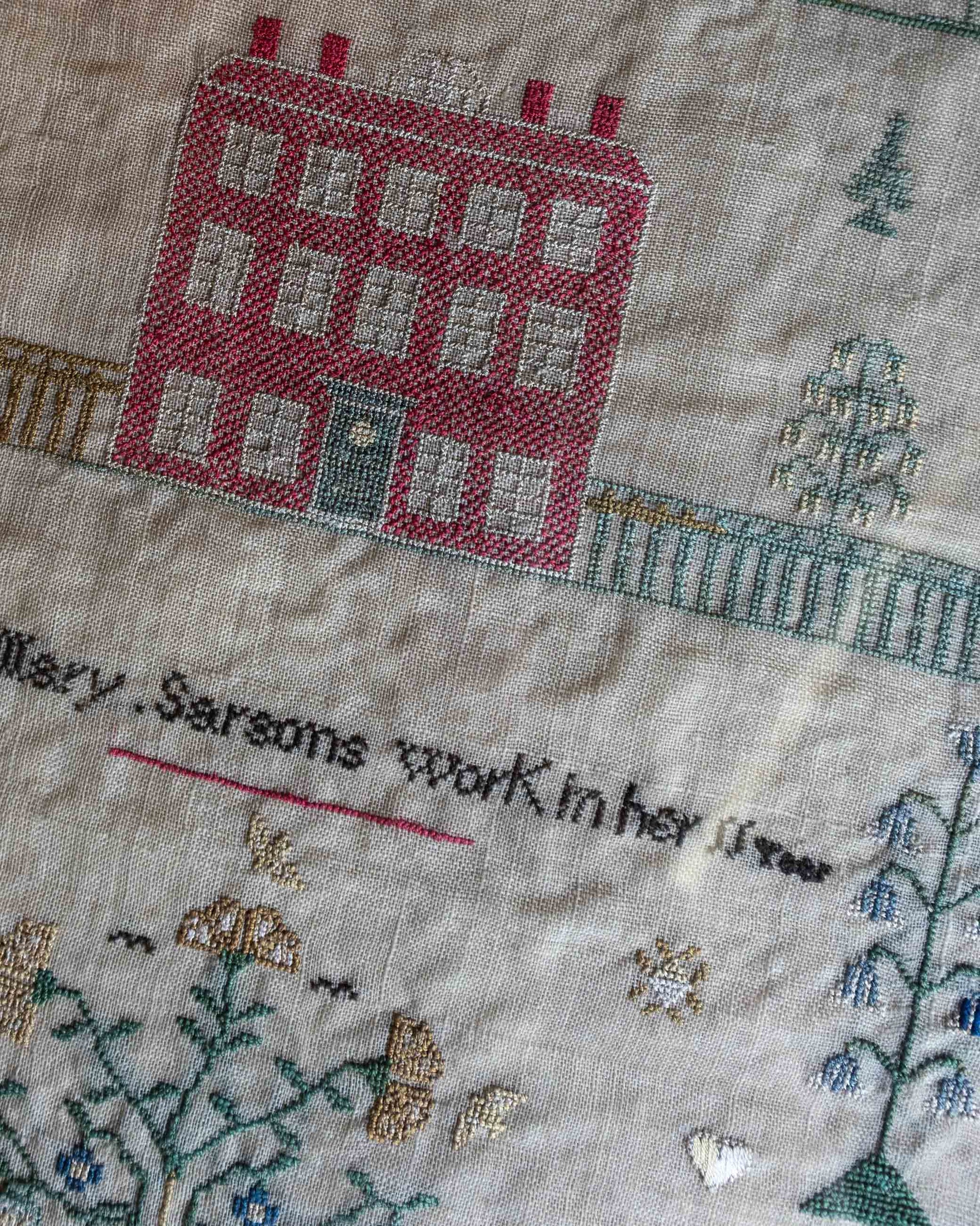 Embroidered cross stitch sampler with a house and text on fabric