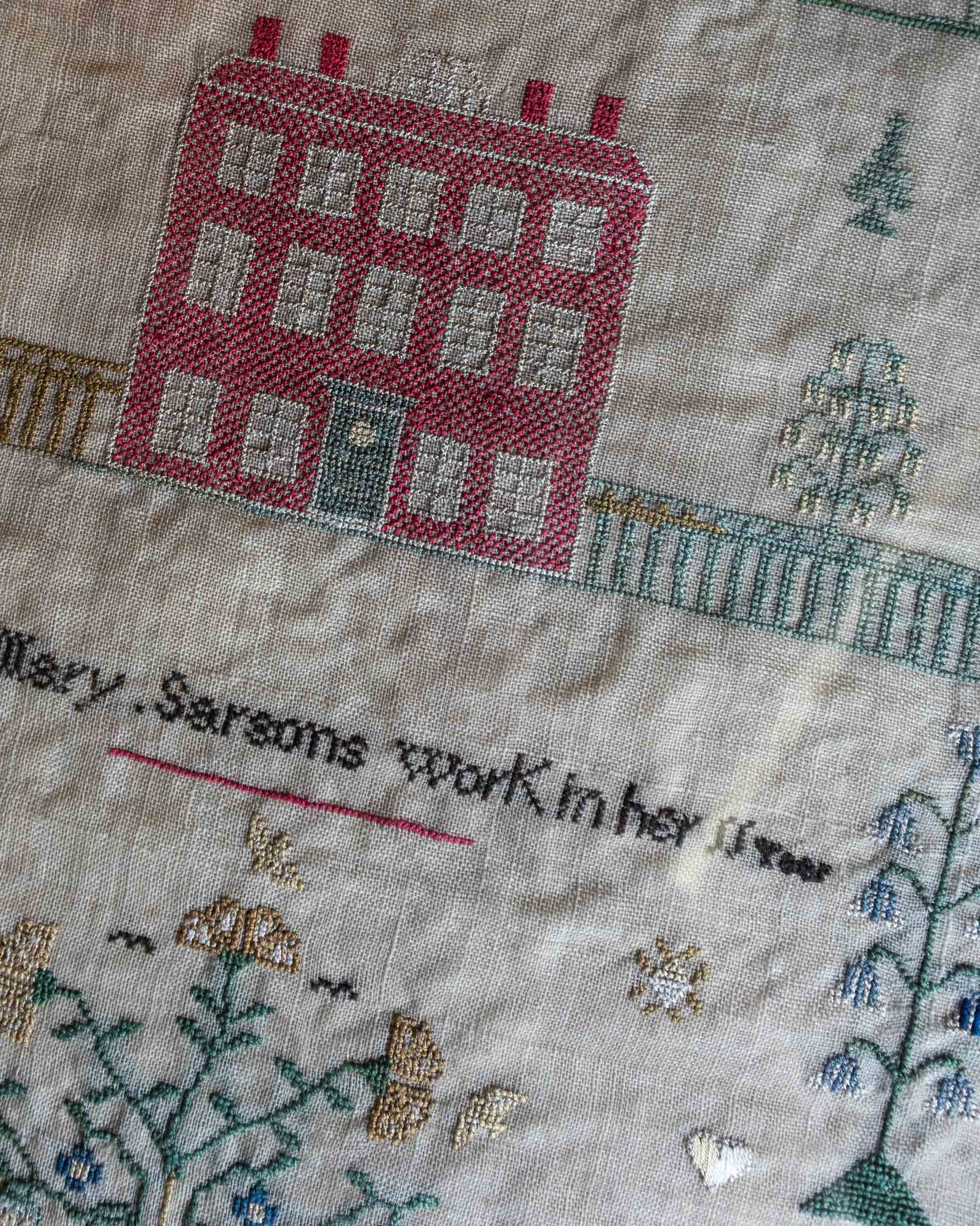 Embroidered cross stitch sampler with a house and text on fabric