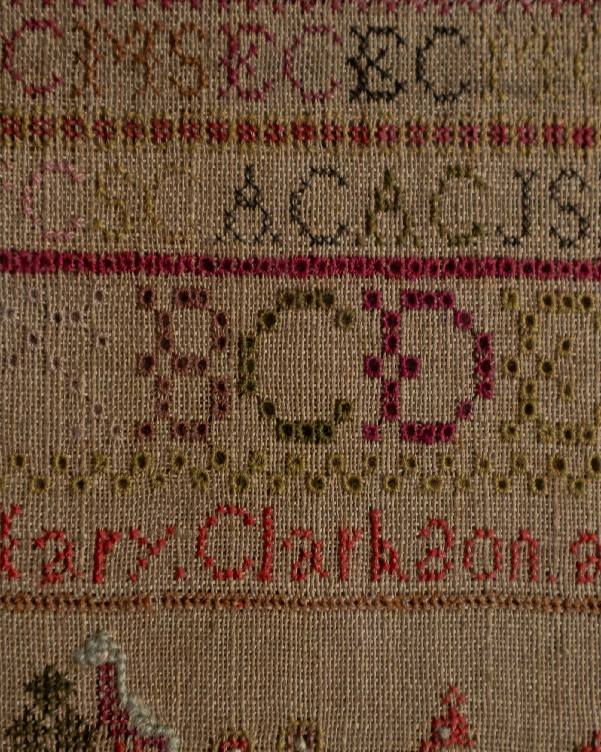 Sampler with embroidered letters and names on a beige background