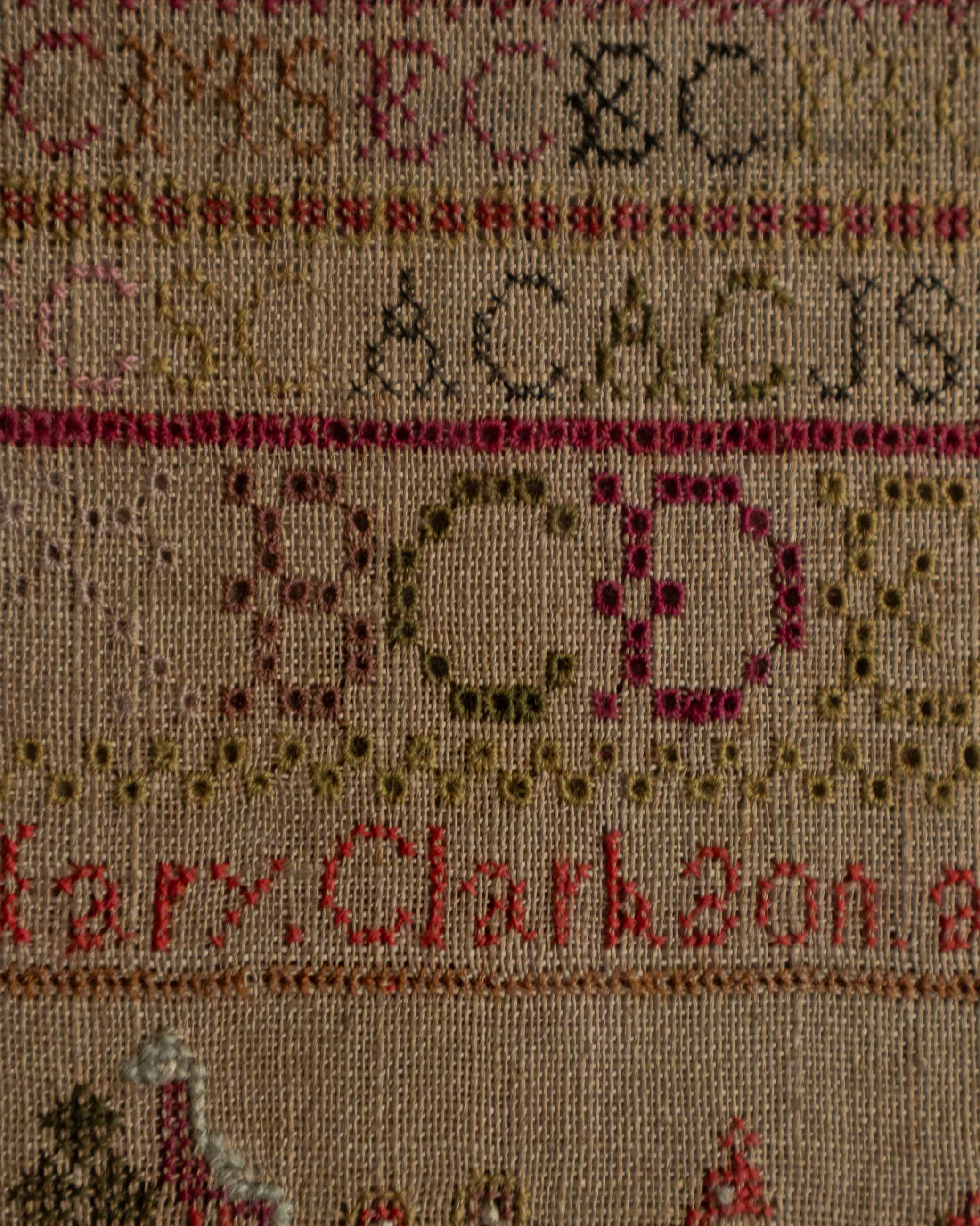 Sampler with embroidered letters and names on a beige background