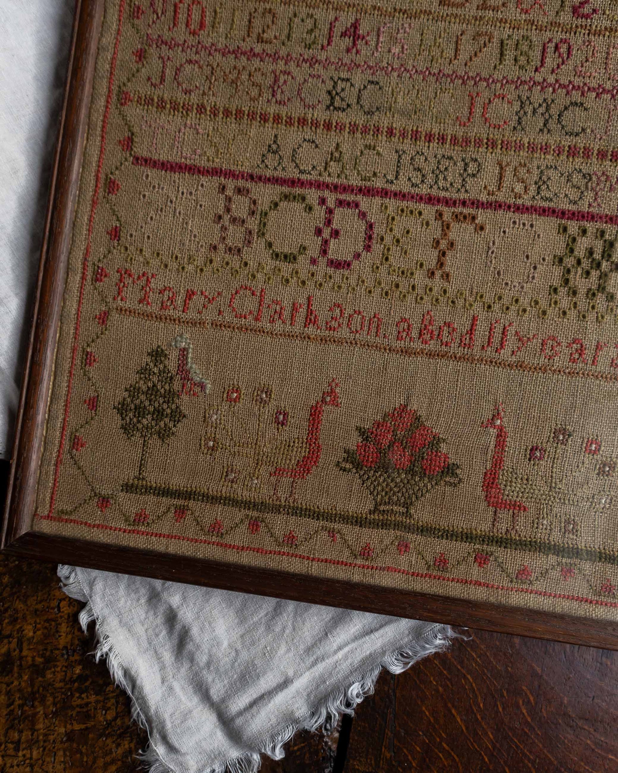 Close-up of a framed embroidered sampler with text and designs on a wooden surface.