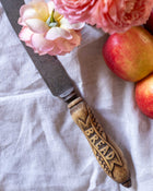 Antique bread knife with decorative handle on a white cloth background, surrounded by flowers and apples.