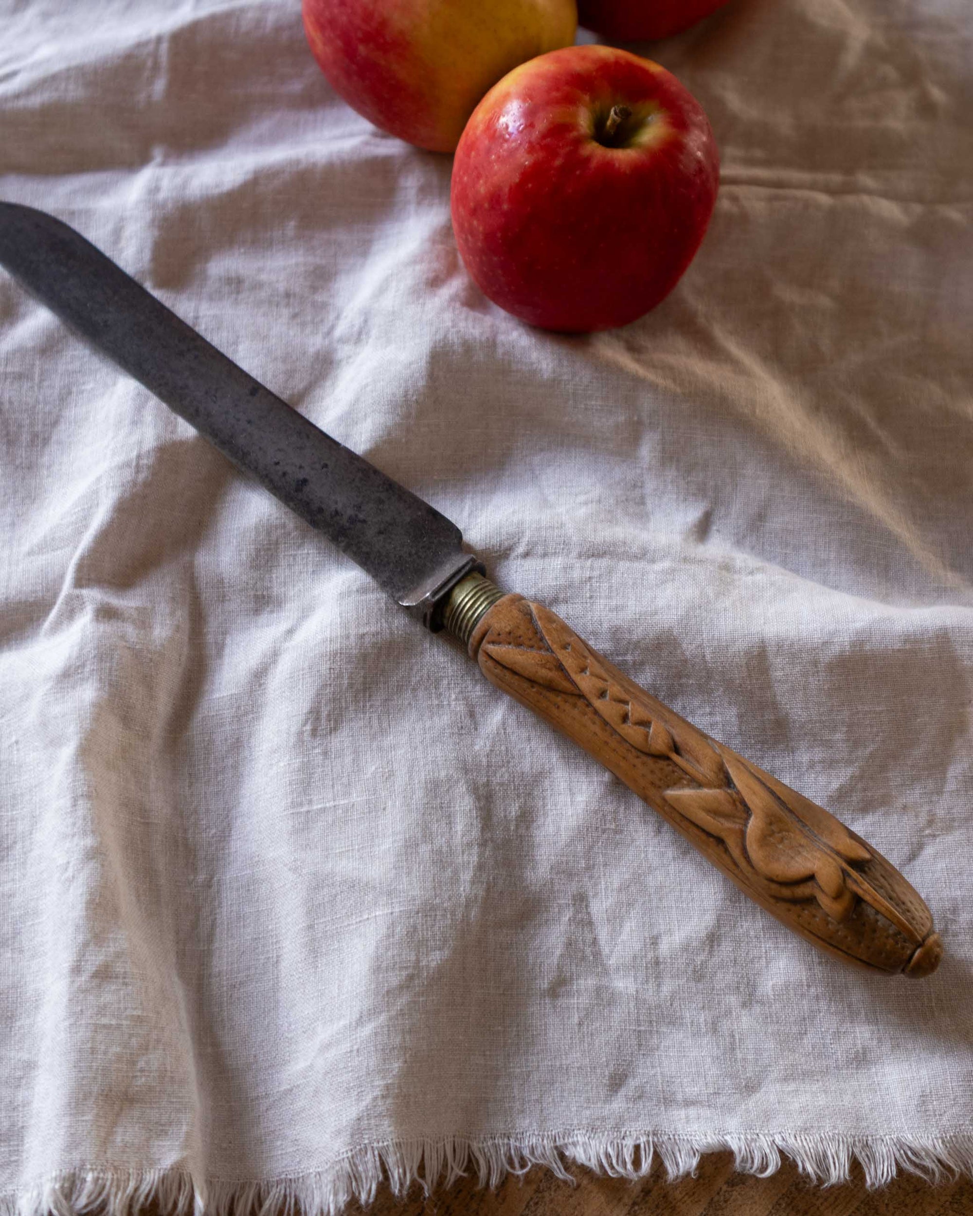 Carved wooden-handled knife on a white cloth with apples in the background