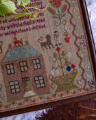 Close-up of a cross-stitched sampler with a house, dog, and cat design.