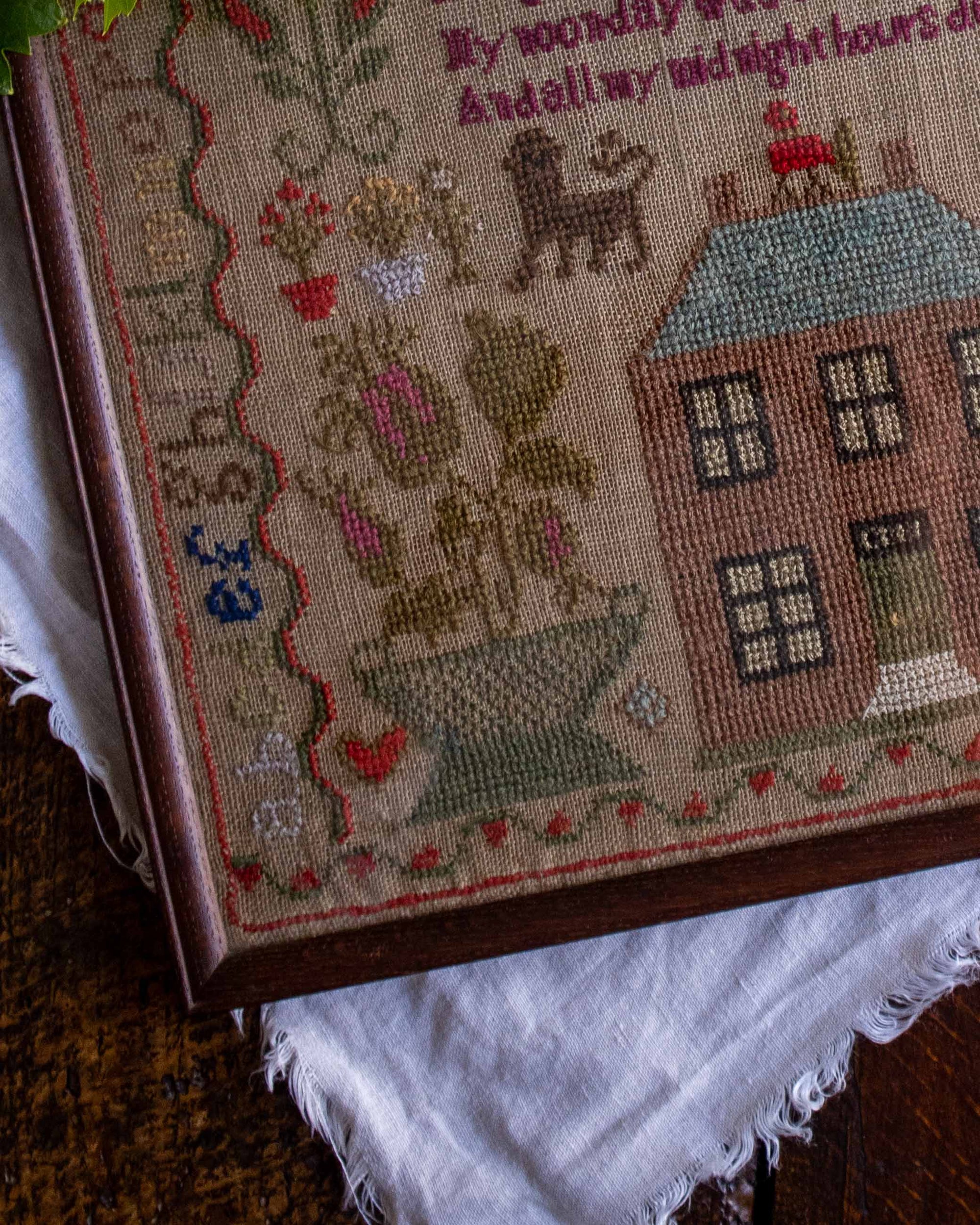 Close-up of a cross stitch antique sampler with a house and cat design on a textured surface.
