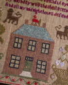 Embroidered sampler scene with a house, cats, and text on a textured background