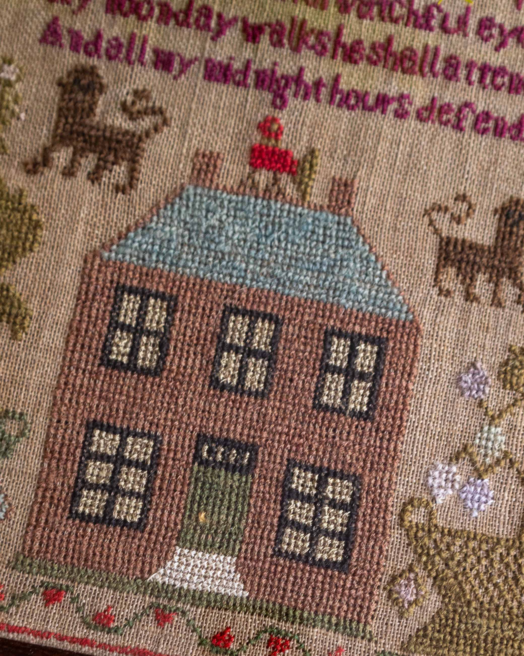 Embroidered sampler scene with a house, cats, and text on a textured background