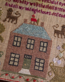 Embroidered sampler scene with a house, cats, and text on a textured background