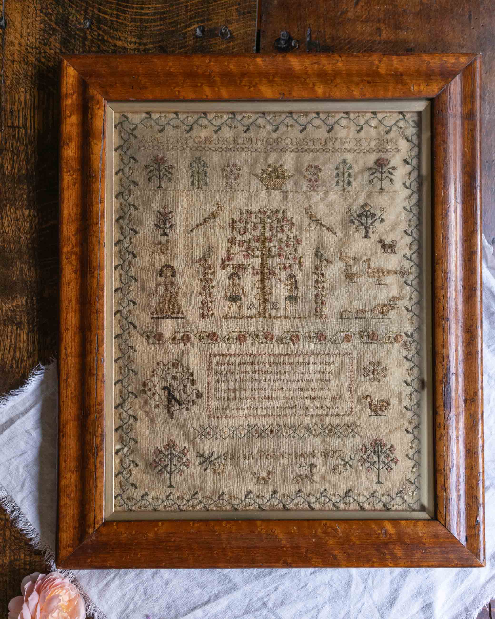 Framed sampler with intricate patterns including Adam and Eve and text on a wooden surface