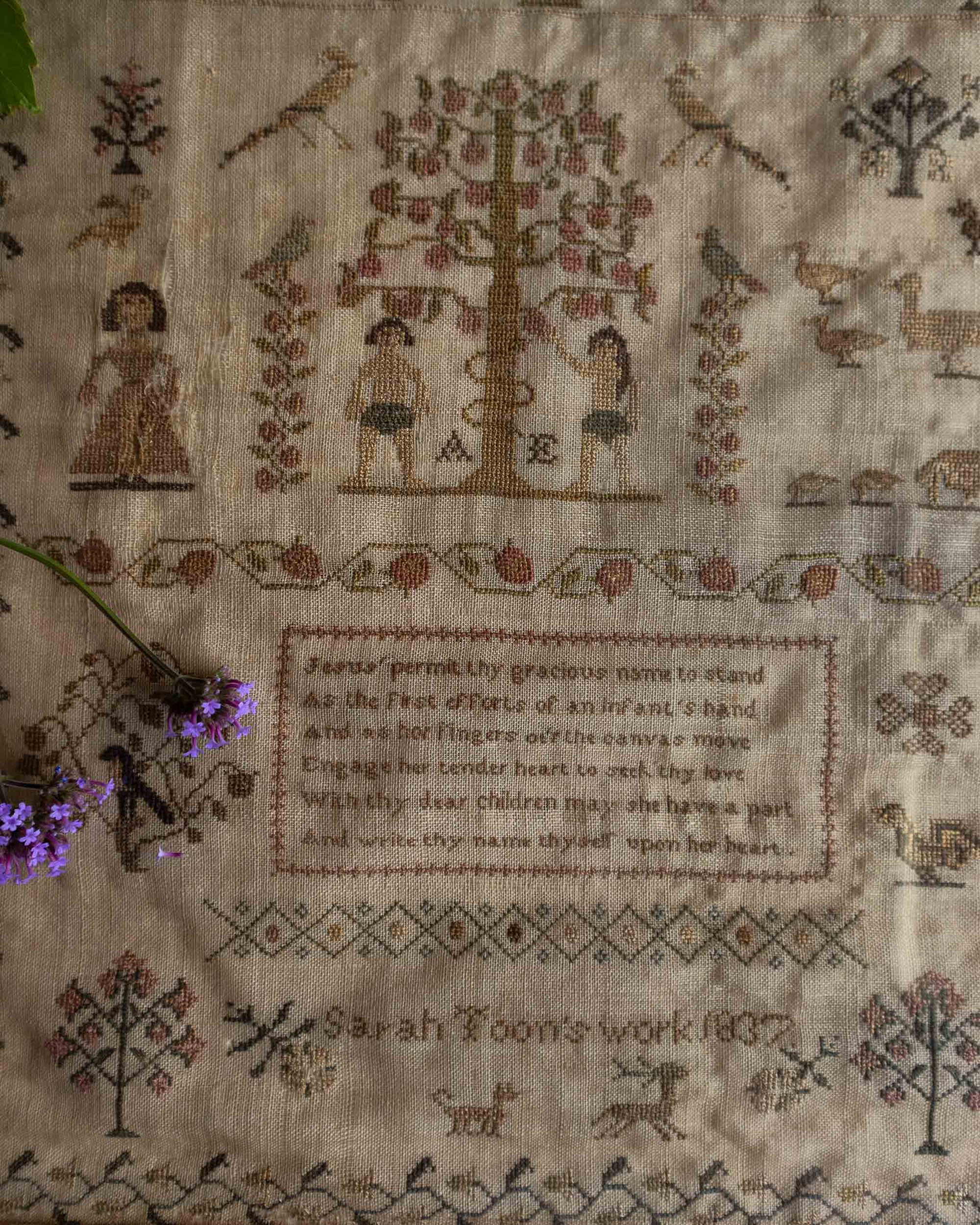 Antique embroidered sampler with text and decorative elements on a beige background